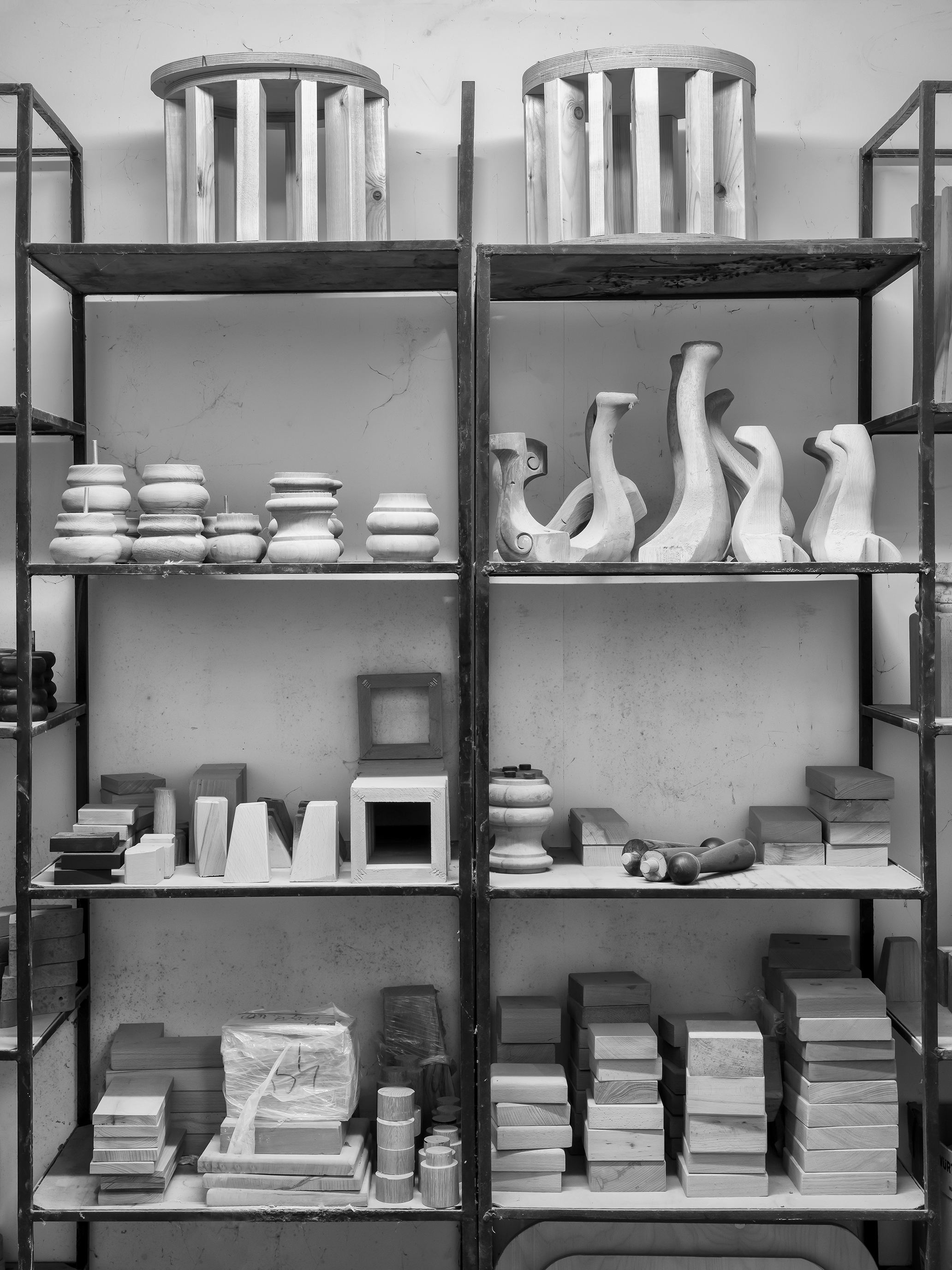 Wooden furniture parts and blocks neatly arranged on metal shelves in a workshop.