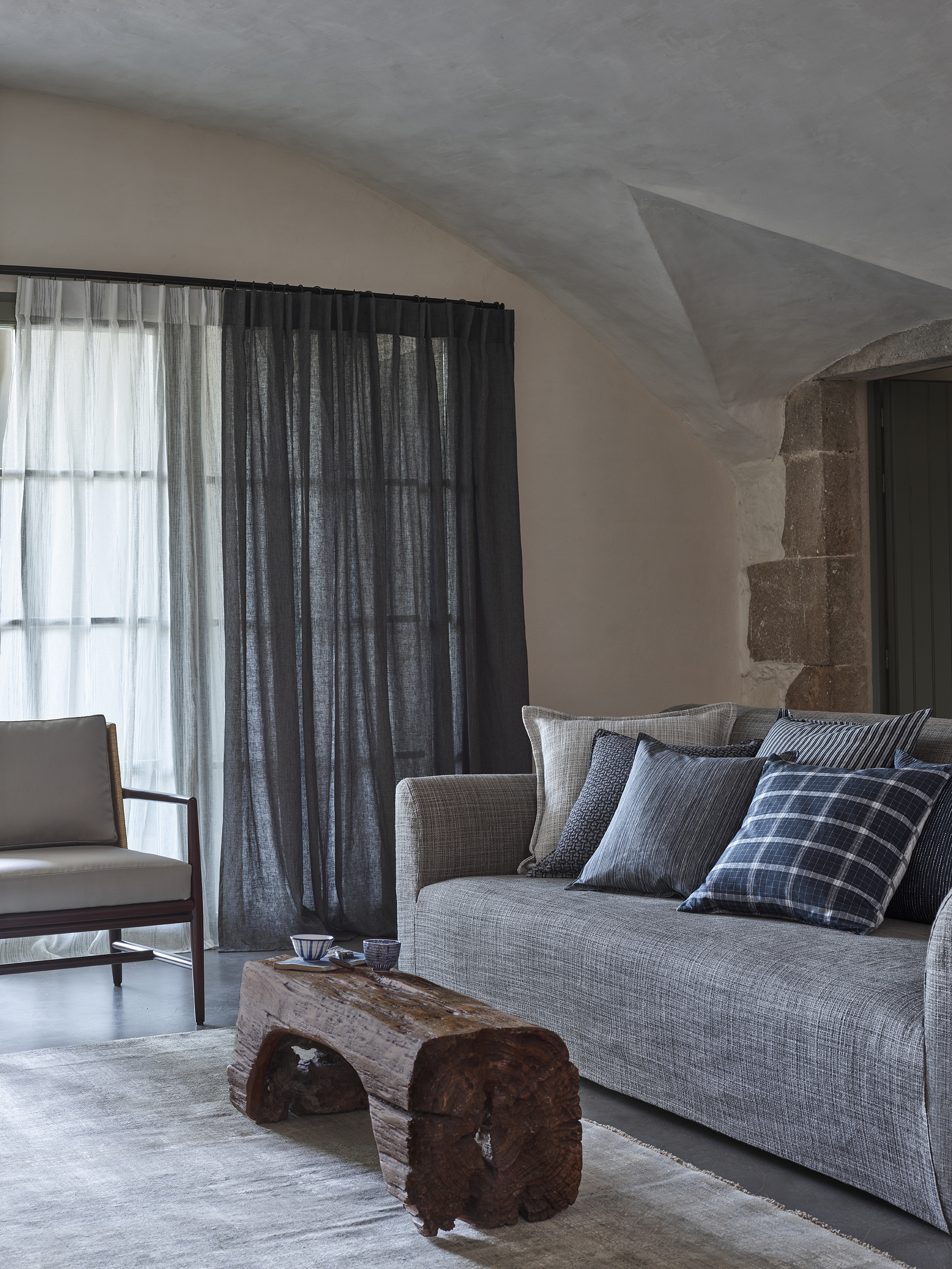 Elegant living room with a Toscana fixed seat sofa by Collett & Victor in textured gray fabric, styled with blue and patterned cushions, complemented by a rustic wooden coffee table and soft natural light.