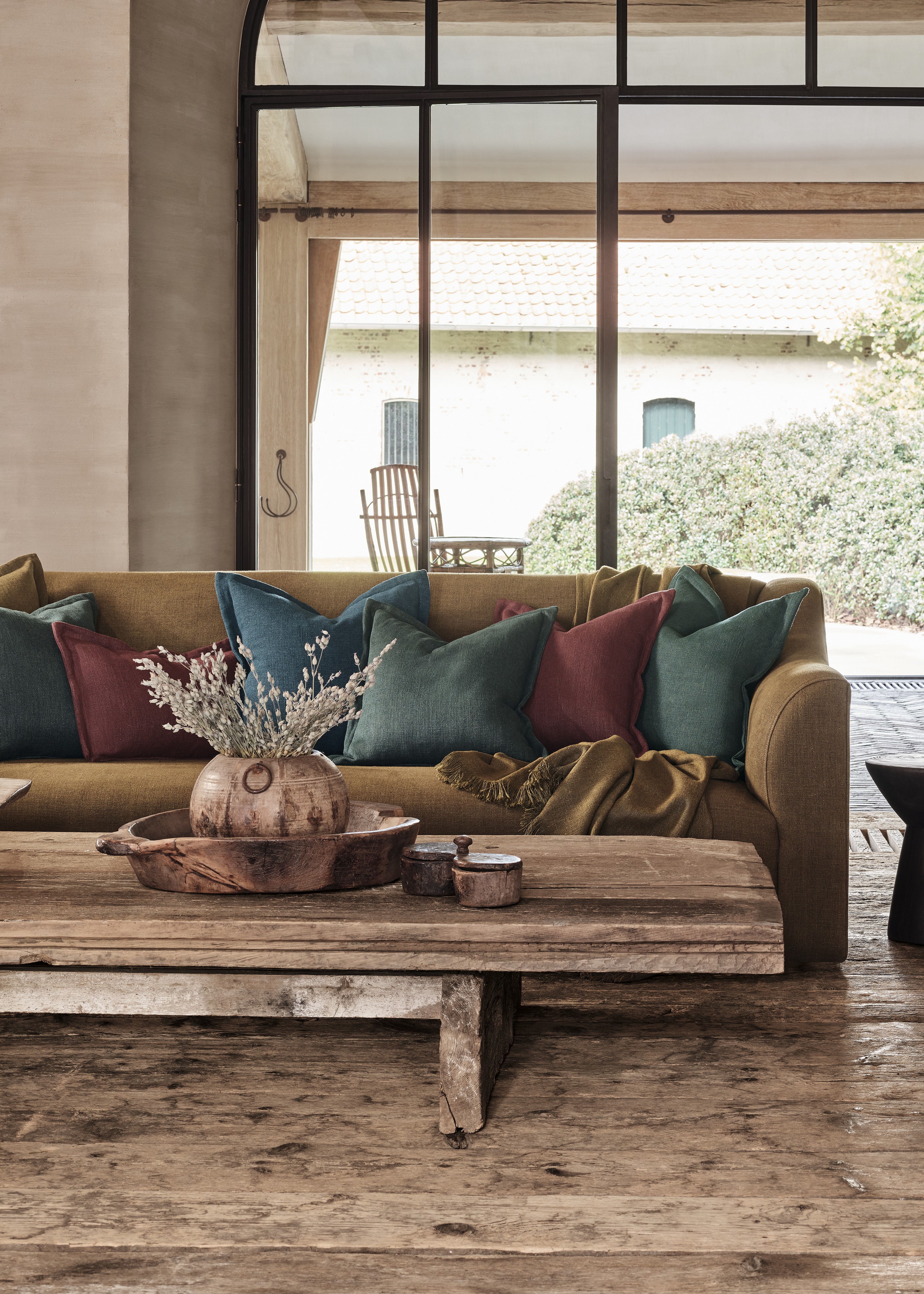 Rustic living room with a Toscana fixed seat sofa by Collett & Victor, styled with jewel-toned cushions, a wooden coffee table, and ceramic decor accents.