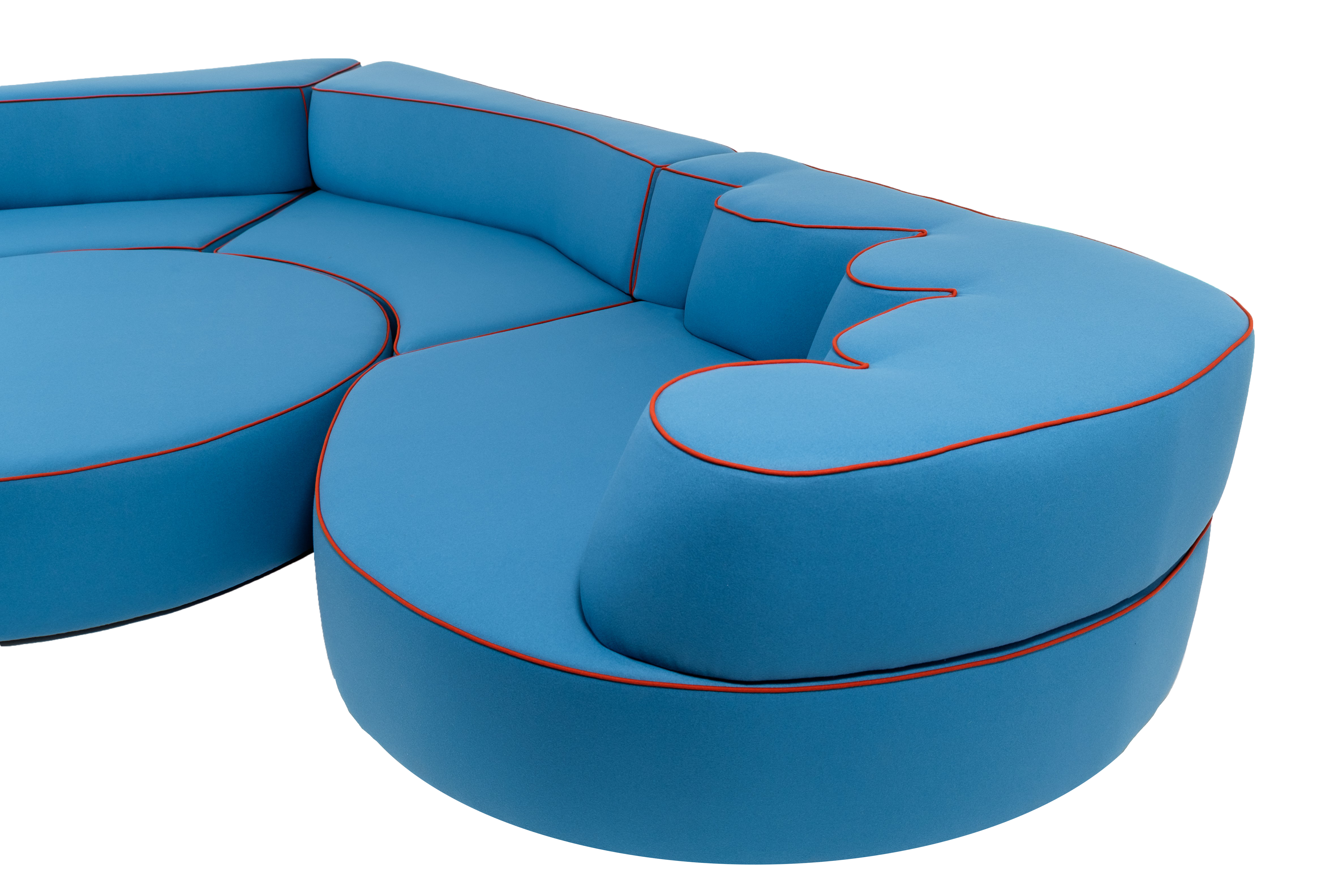 Detail view of the Comporta modular sofa in bright blue upholstery with contrasting red piping, showcasing its sculptural curves and distinctive organic shapes.