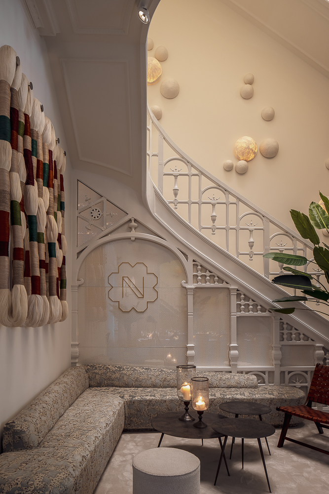 Luxurious hotel lounge with a patterned Collett & Victor sectional sofa, round black coffee tables with candles, and ornate staircase detailing in a refined interior.