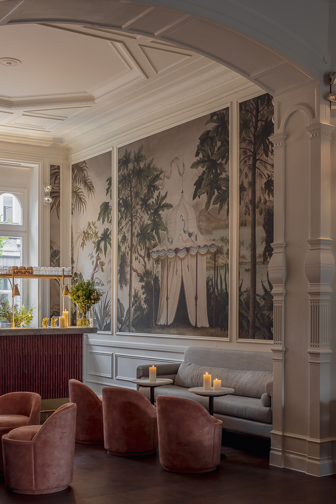 Elegant hotel lounge with bespoke Collett & Victor seating, featuring blush velvet chairs, a grey sofa, and a hand-painted mural in a refined interior.