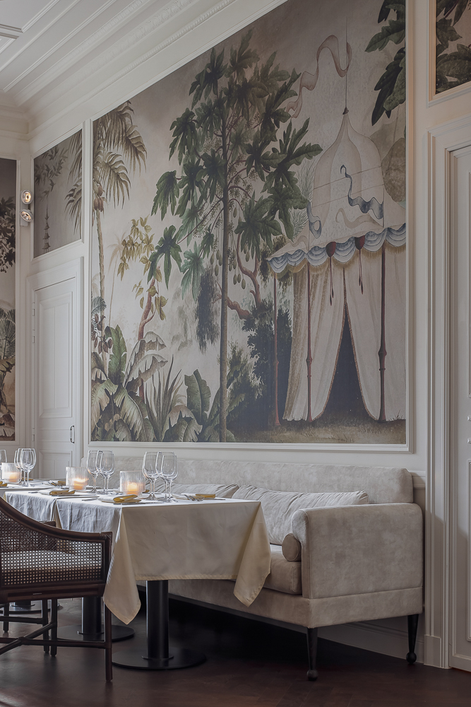 Refined restaurant corner at The Nine Hotel with mural wall art, elegant table setting, and a plush upholstered banquette.