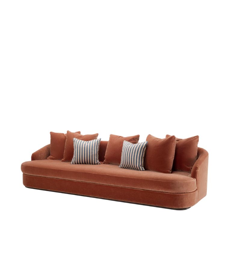 Low, rounded Elly sofa upholstered in rust-colored fabric, featuring six matching rust-colored cushions and three contrasting blue-and-white striped cushions, set against a white background.