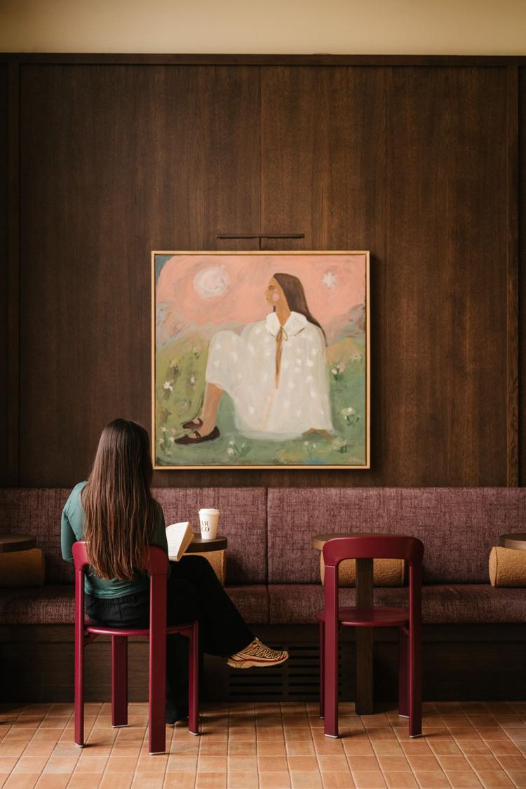 Woman sat, reading a book with a coffee on the table at Dear Coco