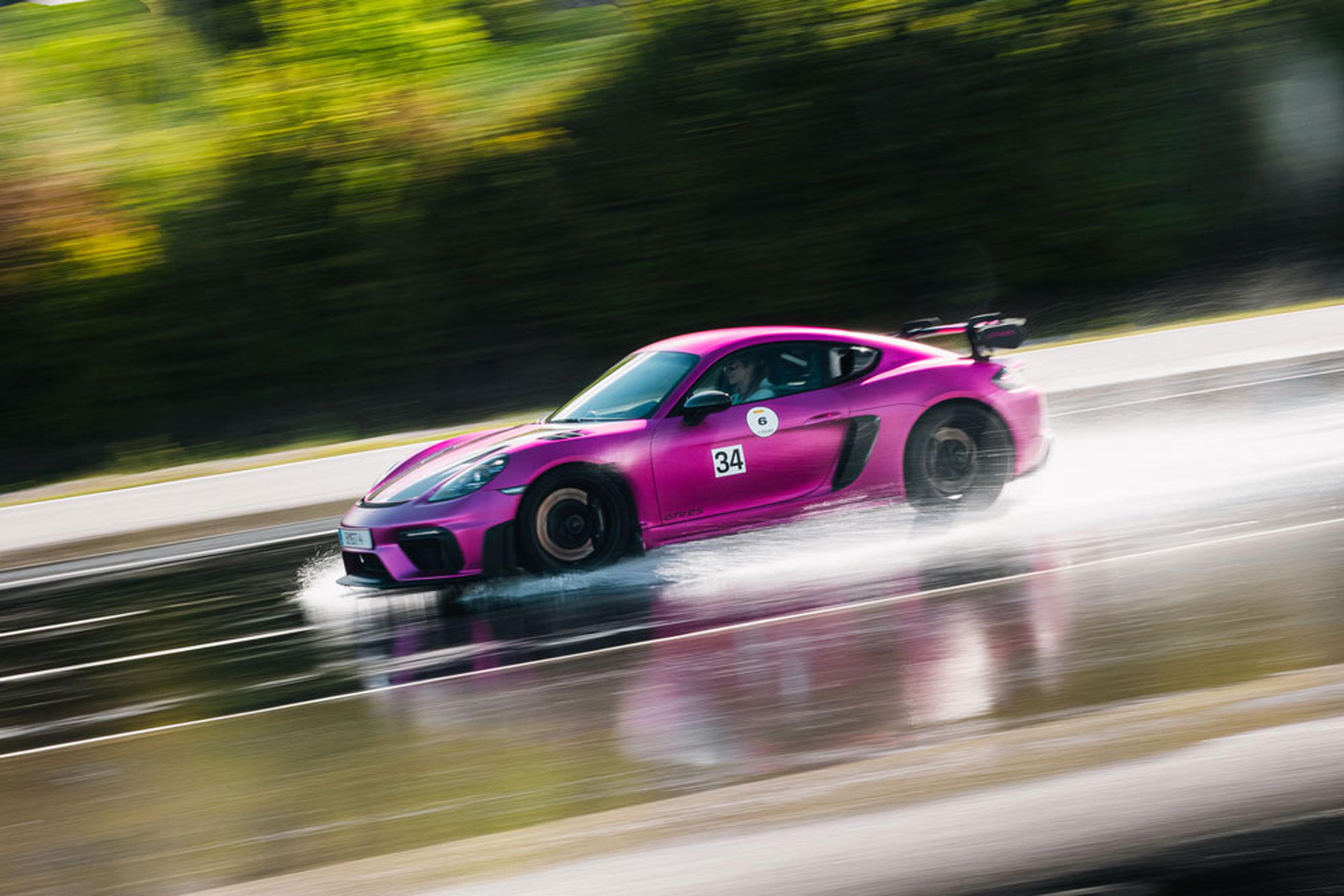 Ein leuchtend pinkfarbener Sportwagen rast über eine nasse Rennstrecke, wobei er Wasser aufwirbelt; im Hintergrund ist die Vegetation nur noch schemenhaft zu erkennen.