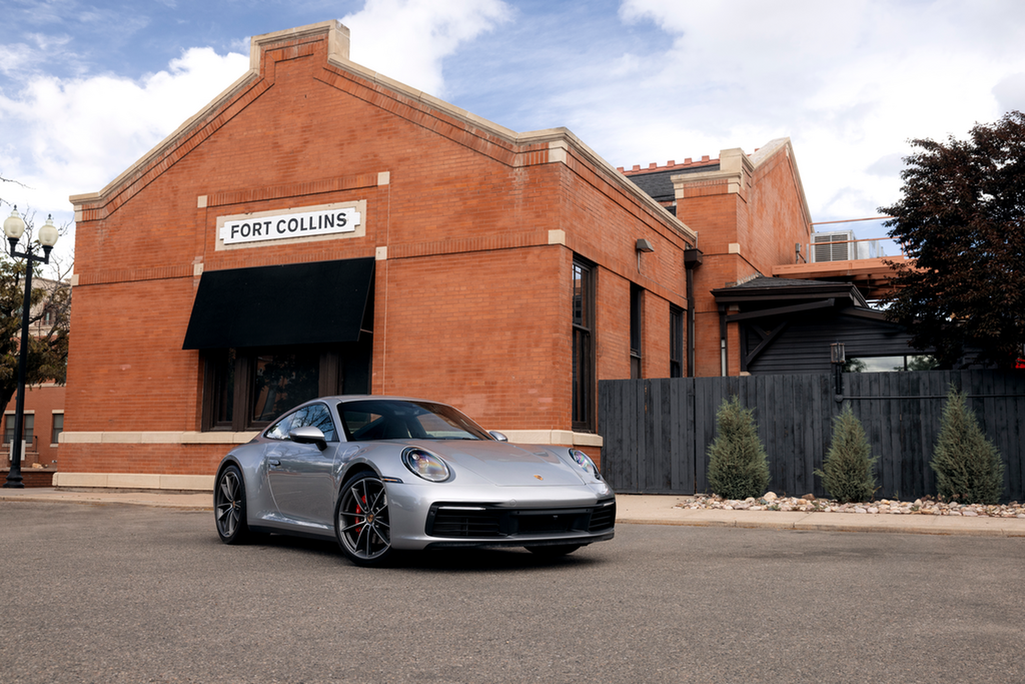 A silver sports car parked in front of a red brick building with a sign reading "Fort Collins."
