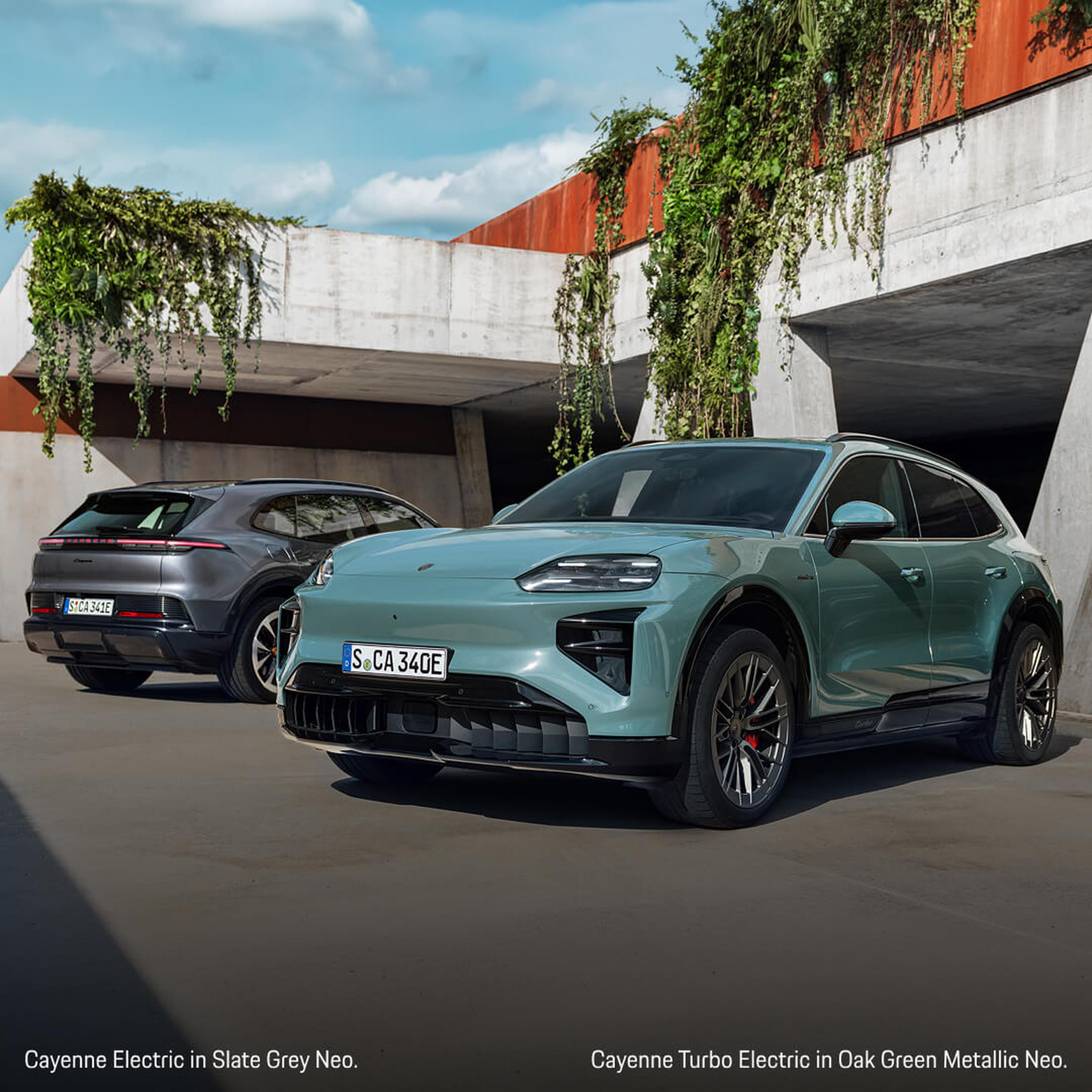 Front three-quarter view of a Porsche Cayenne Electric in Grey and Turbo Electric in Green parked.