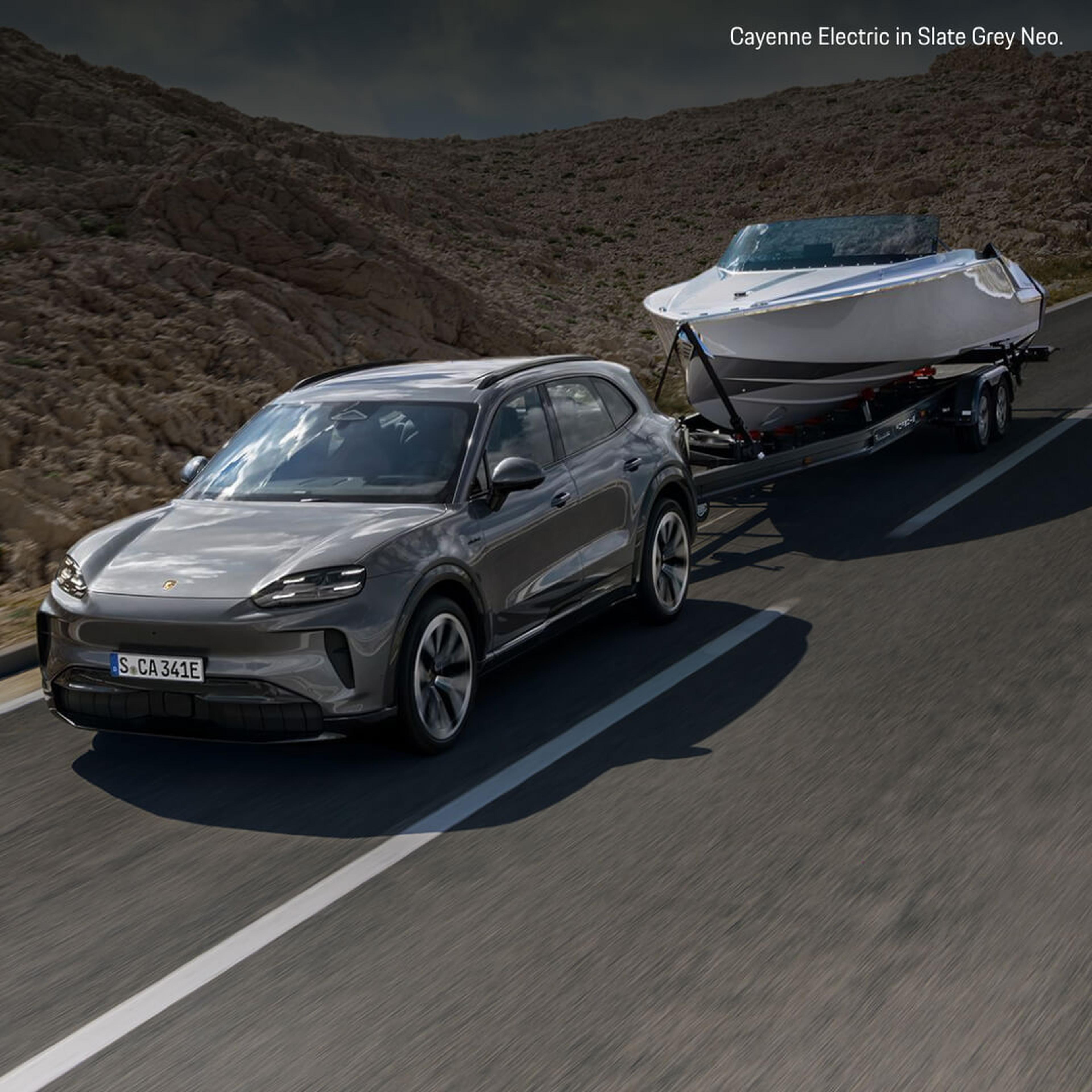 Front three-quarter view of a grey Porsche Cayenne Electric towing a white luxury speedboat.