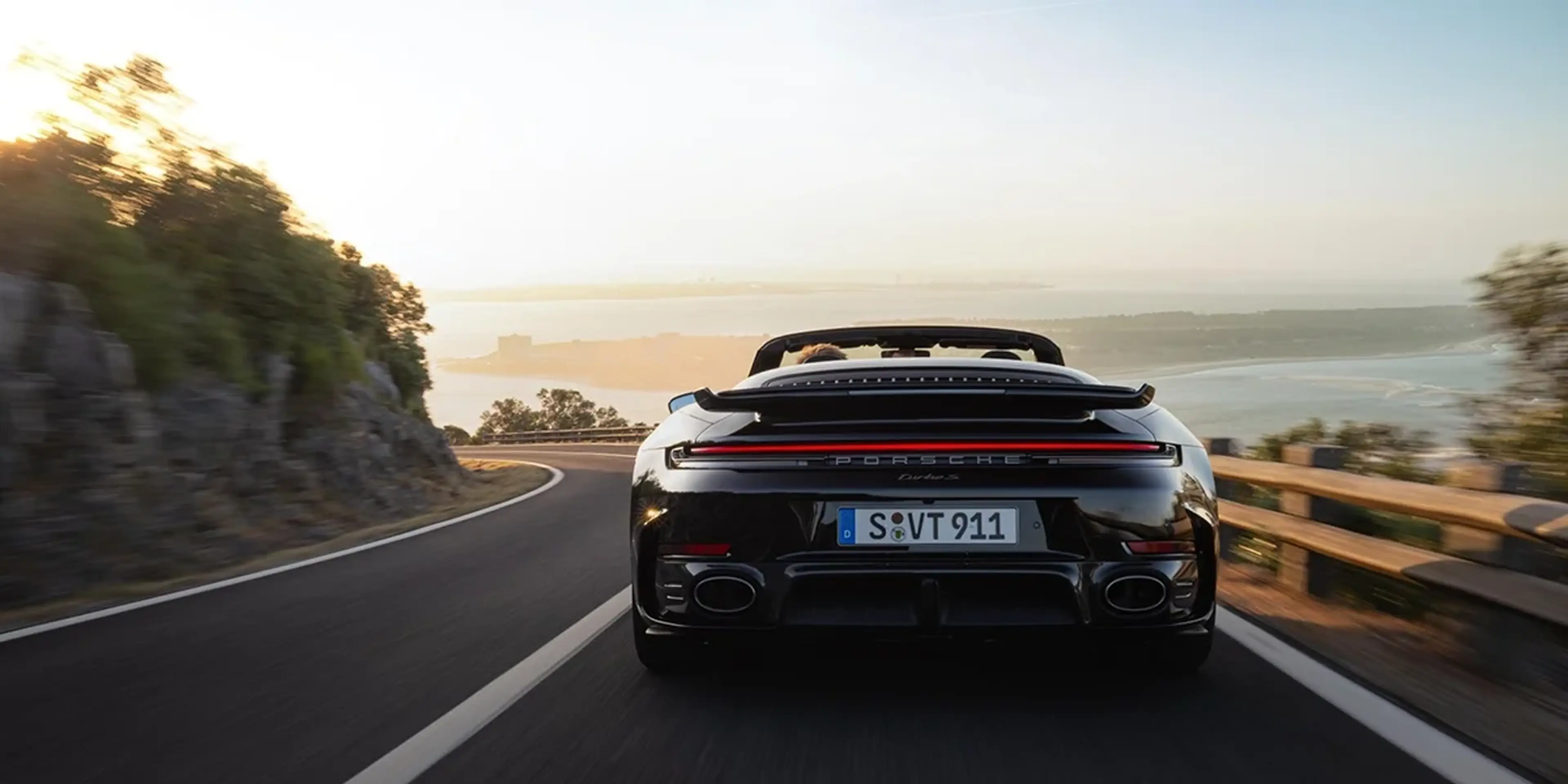 Side profile of a Porsche 911 Turbo S Cabriolet in a studio with a white backdrop, red convertible top folded.