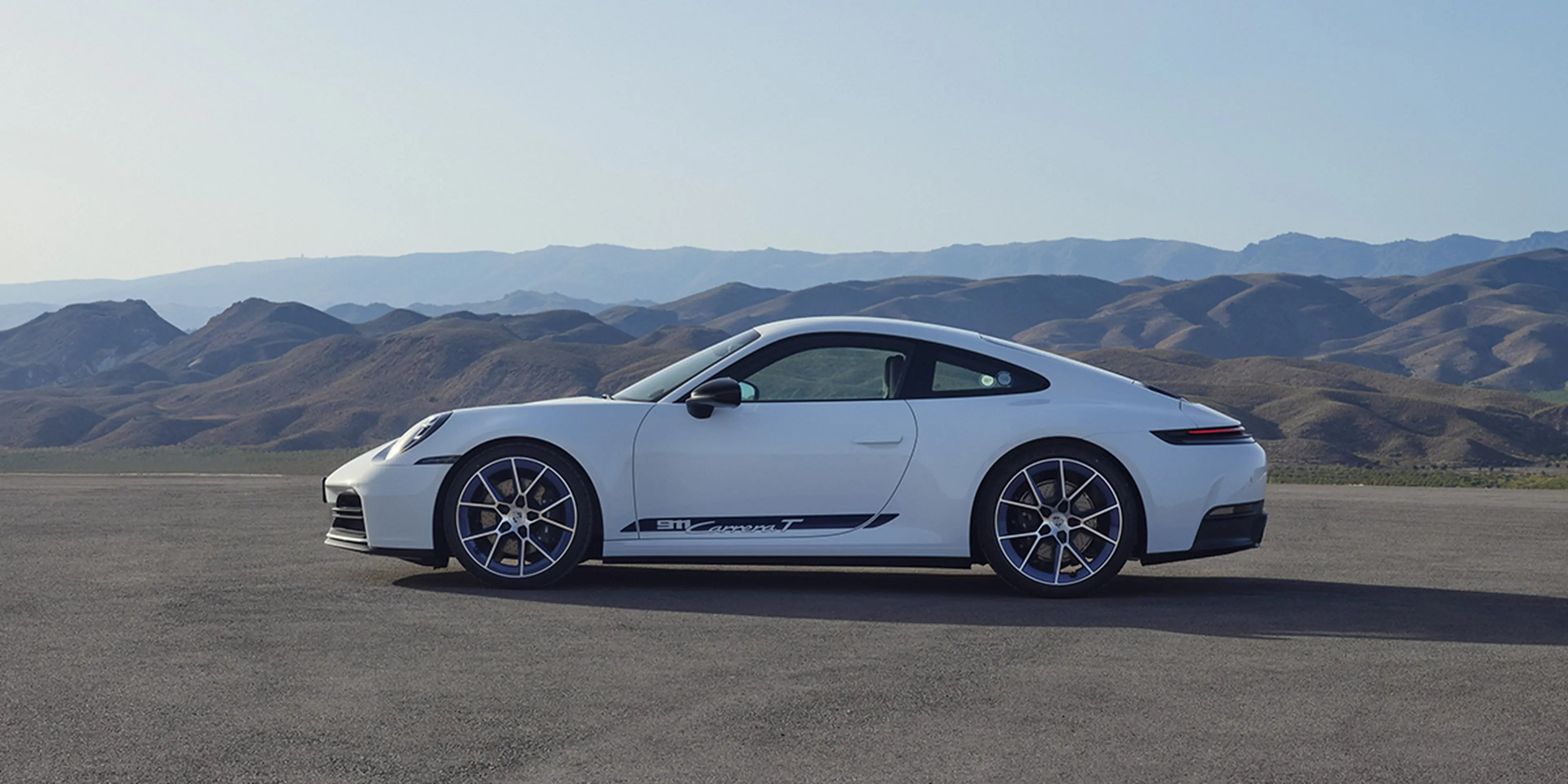 White 2025 Porsche 911 Carrera T side profile on a coastal road