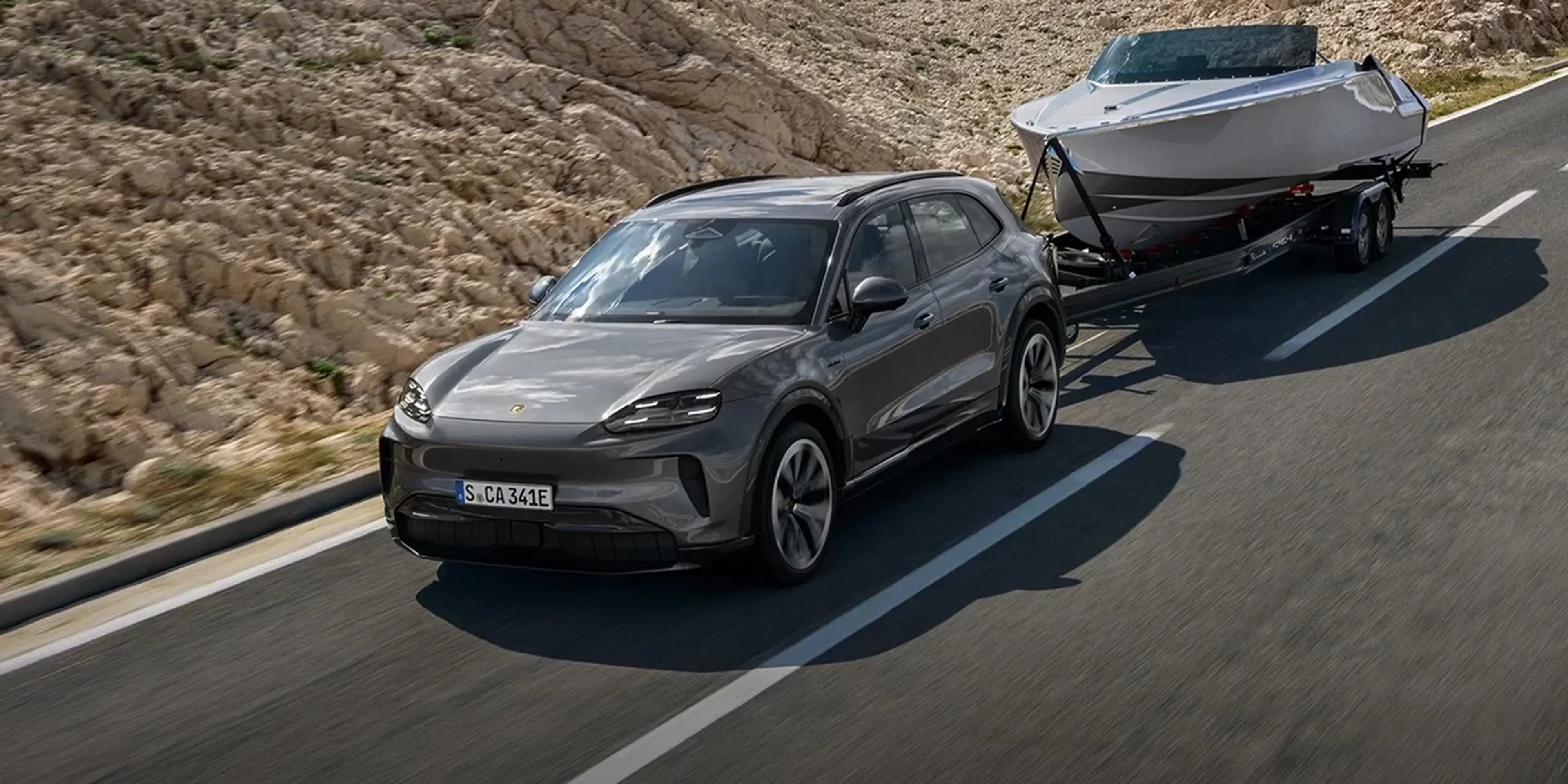 Porsche Cayenne towing a large boat trailer on a highway, demonstrating strong towing performance.