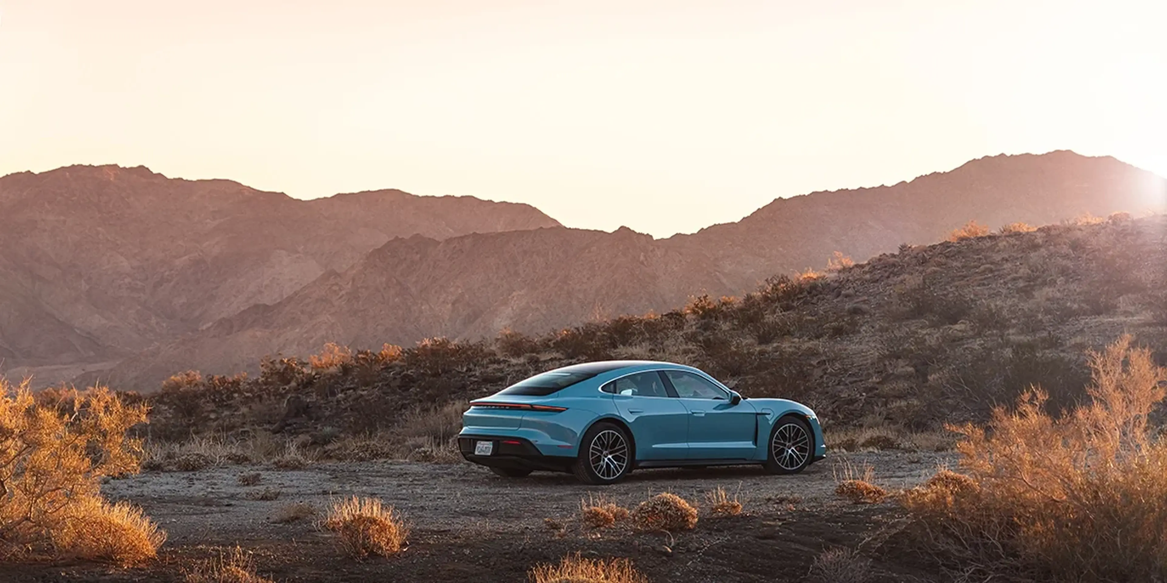 Porsche Taycan 4S rear three-quarter view in desert landscape, Frozen Blue