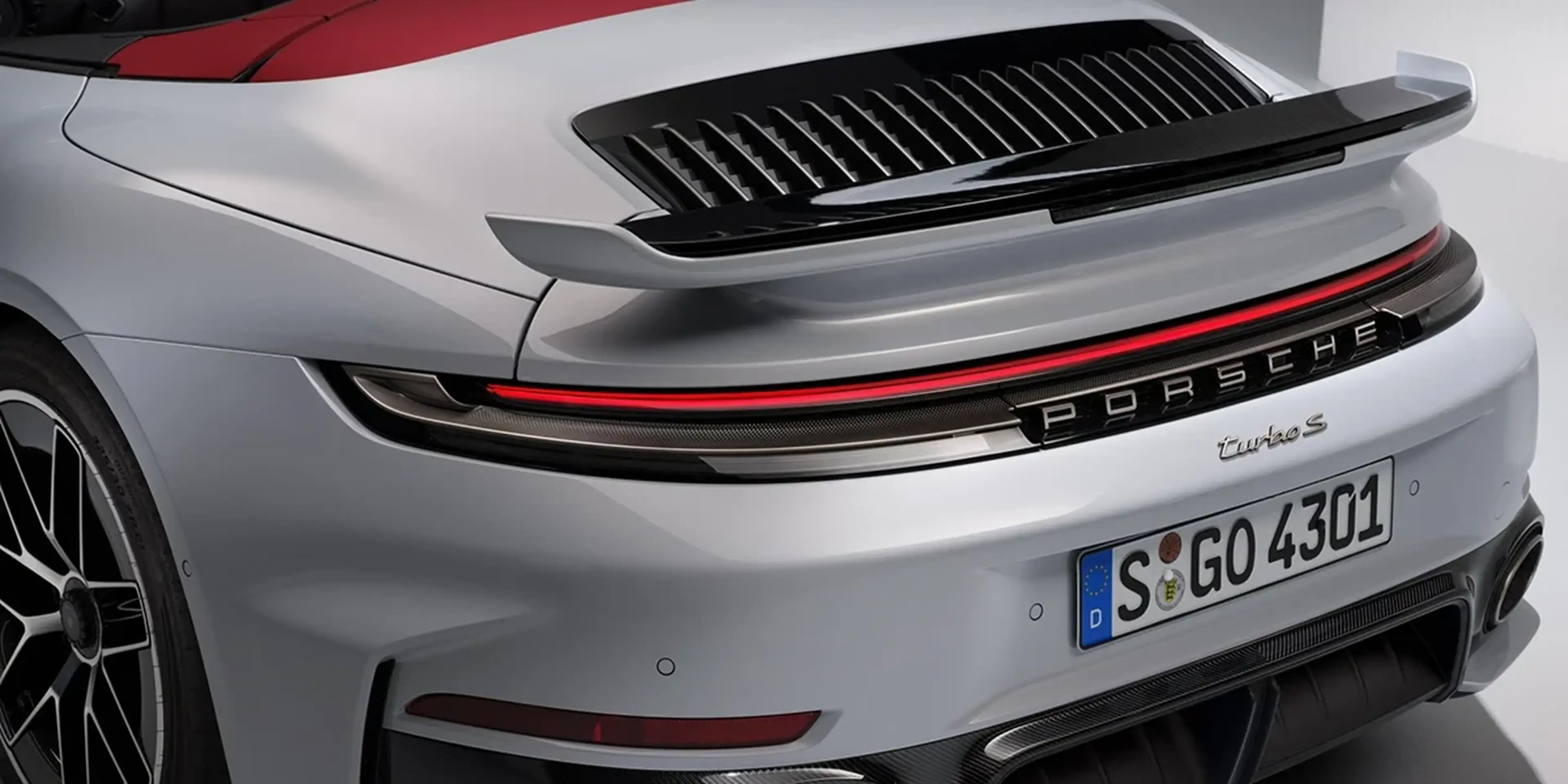Rear view of Porsche 911 Turbo S Cabriolet driving on a curving mountain road at sunset.