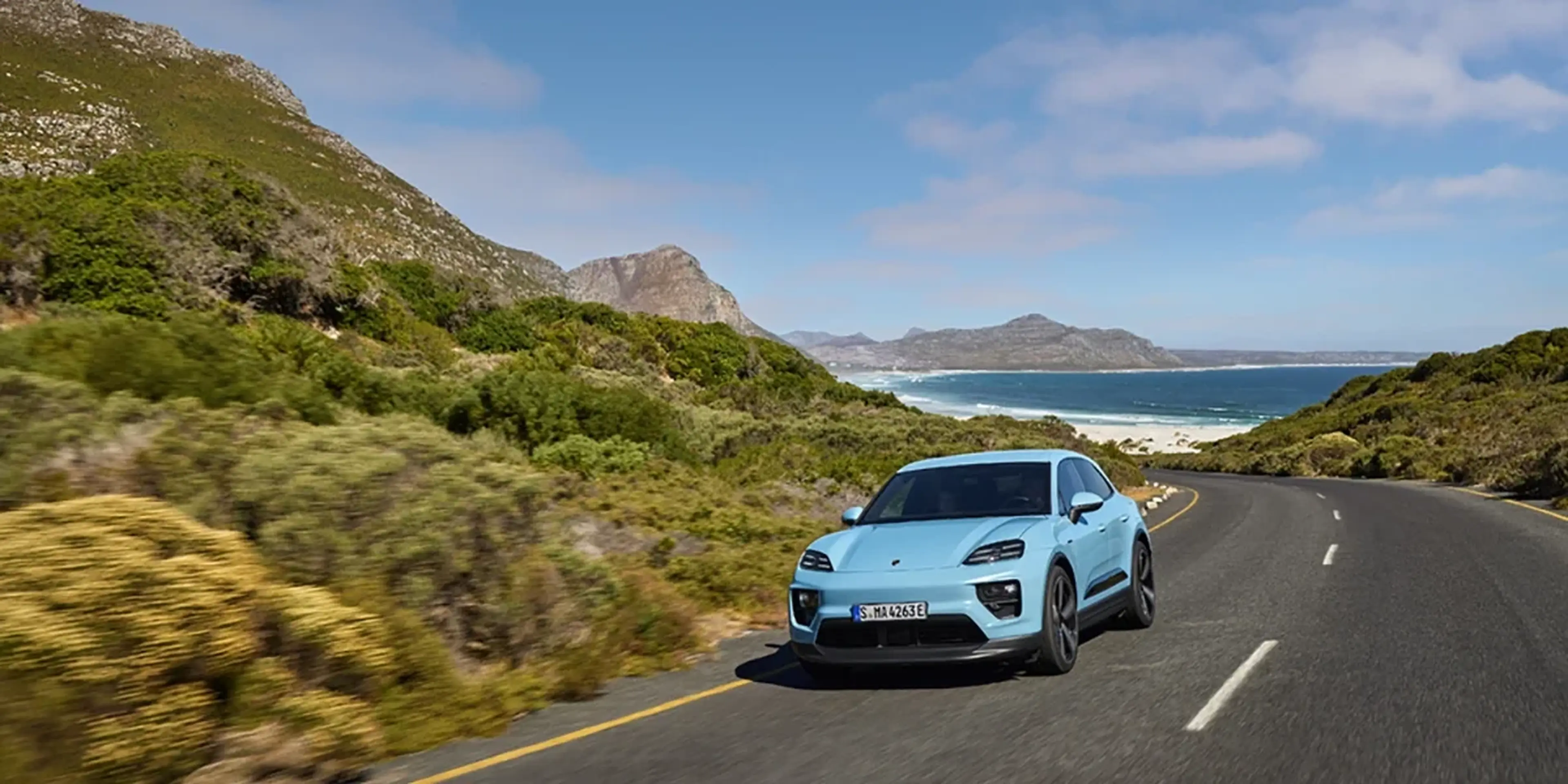 Blue Porsche Macan T parked near harbor with a Mediterranean town in the background