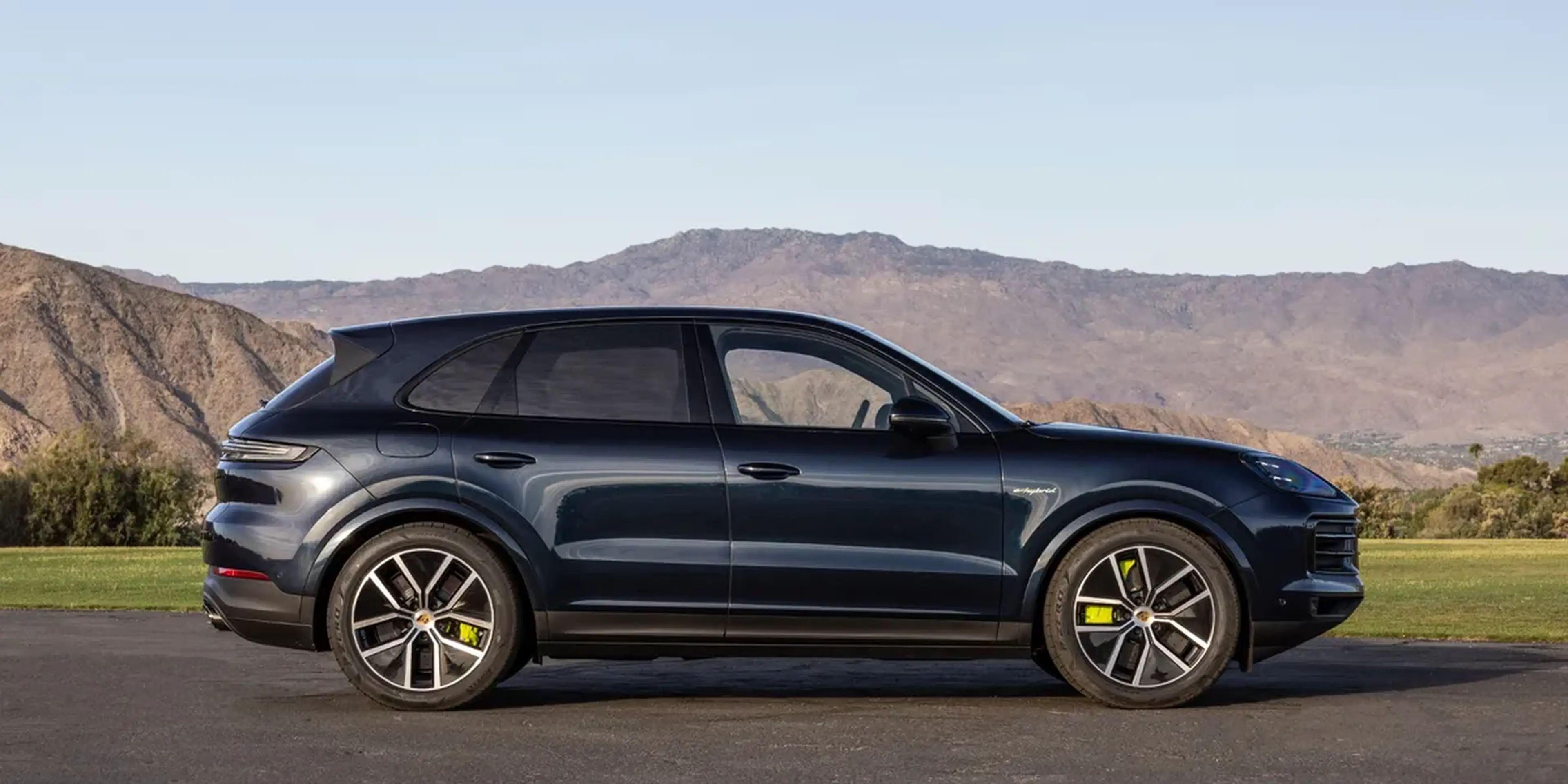 Side profile of the Porsche Cayenne E-Hybrid parked with mountains in the backdrop.