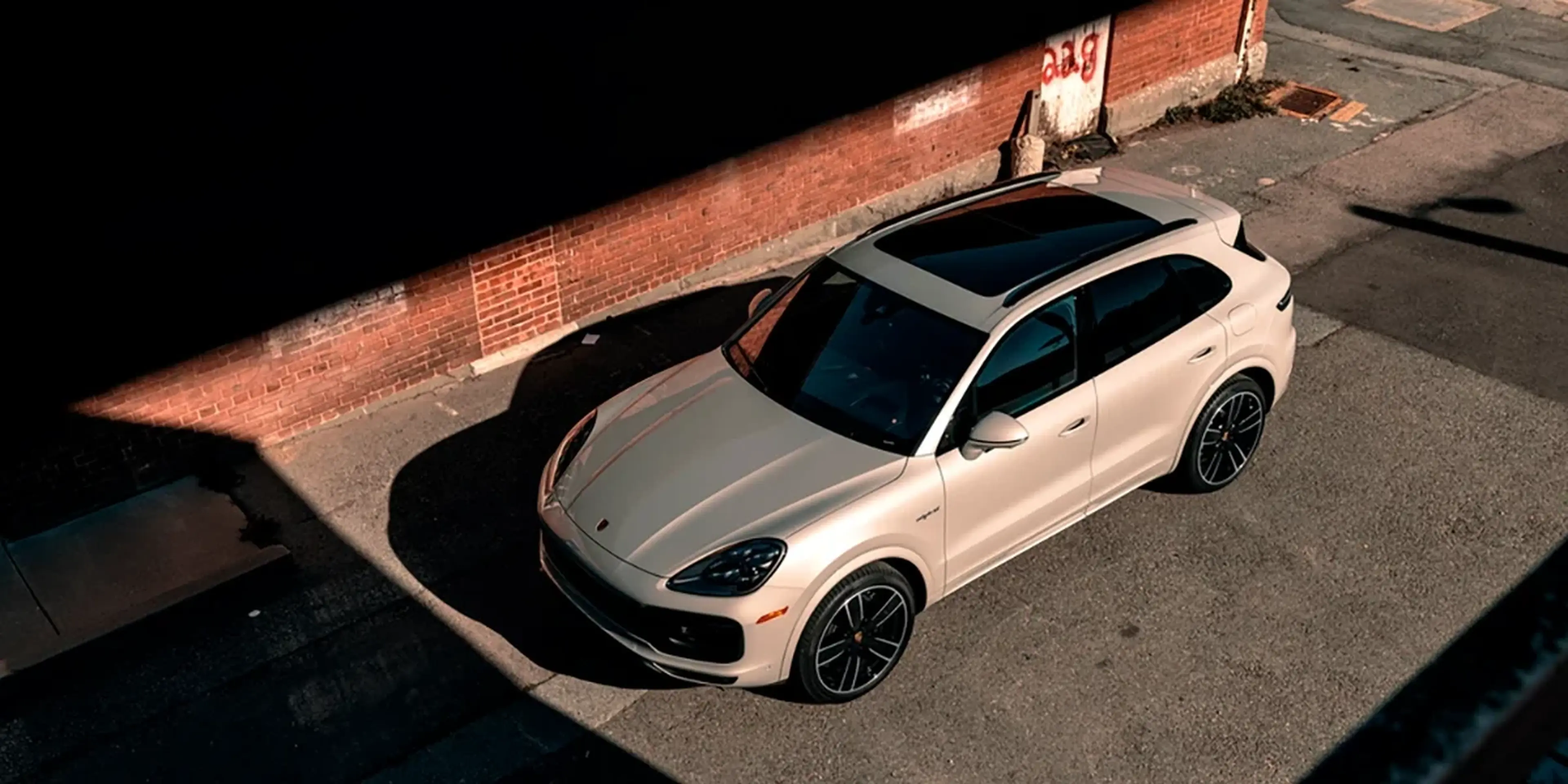 Overhead view of a white Porsche Cayenne parked by a brick wall