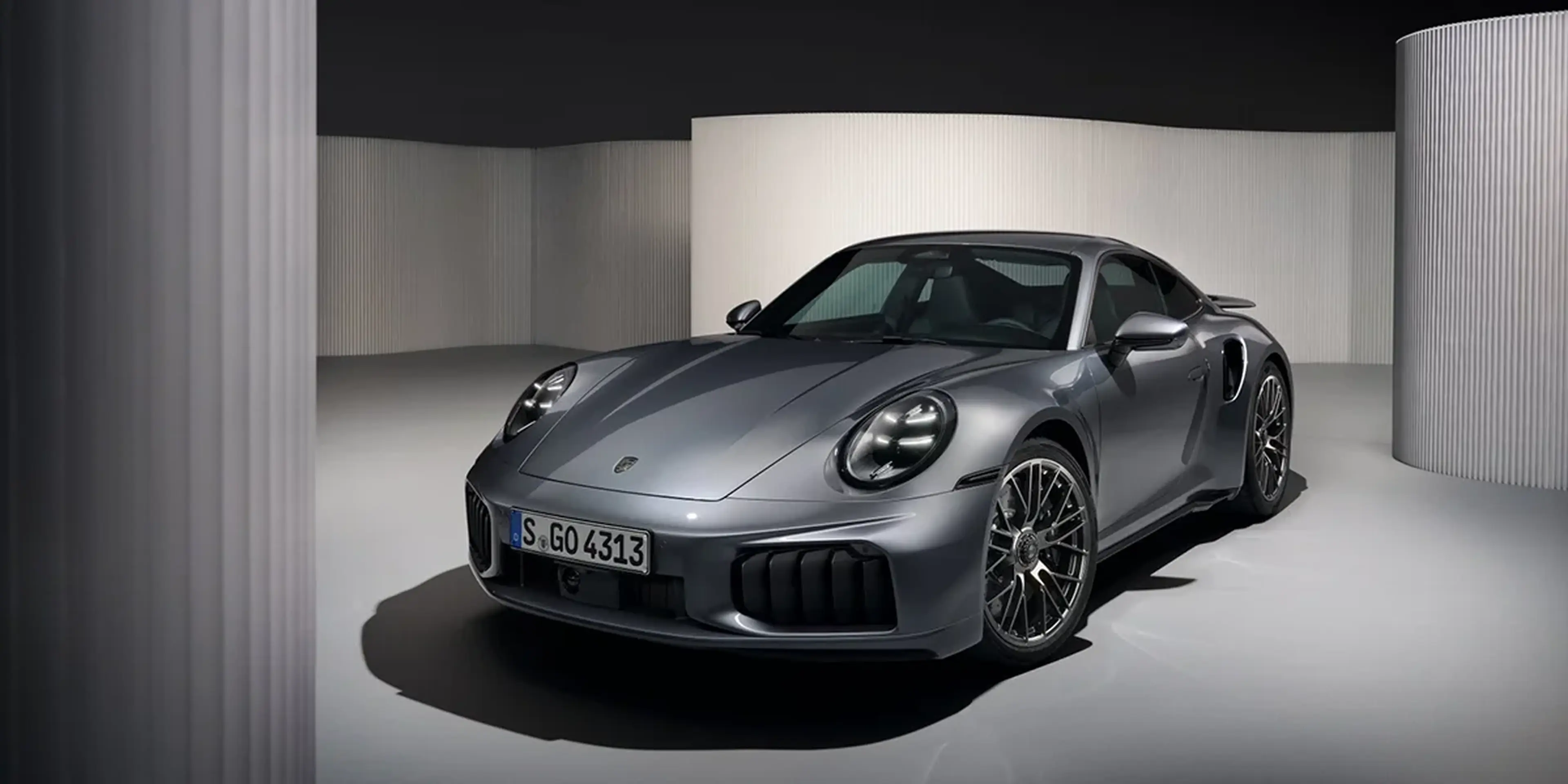 Front view of 2026 Porsche 911 Turbo S coupe in metallic gray with aggressive bumper design.