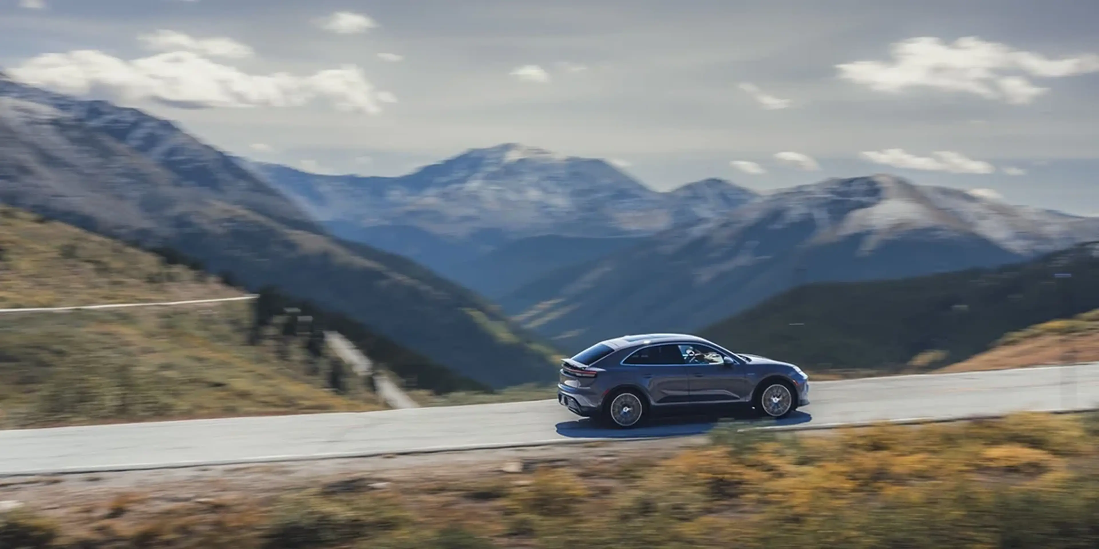 Porsche Macan 4S driving along a mountain road, demonstrating dynamic performance and agility.
