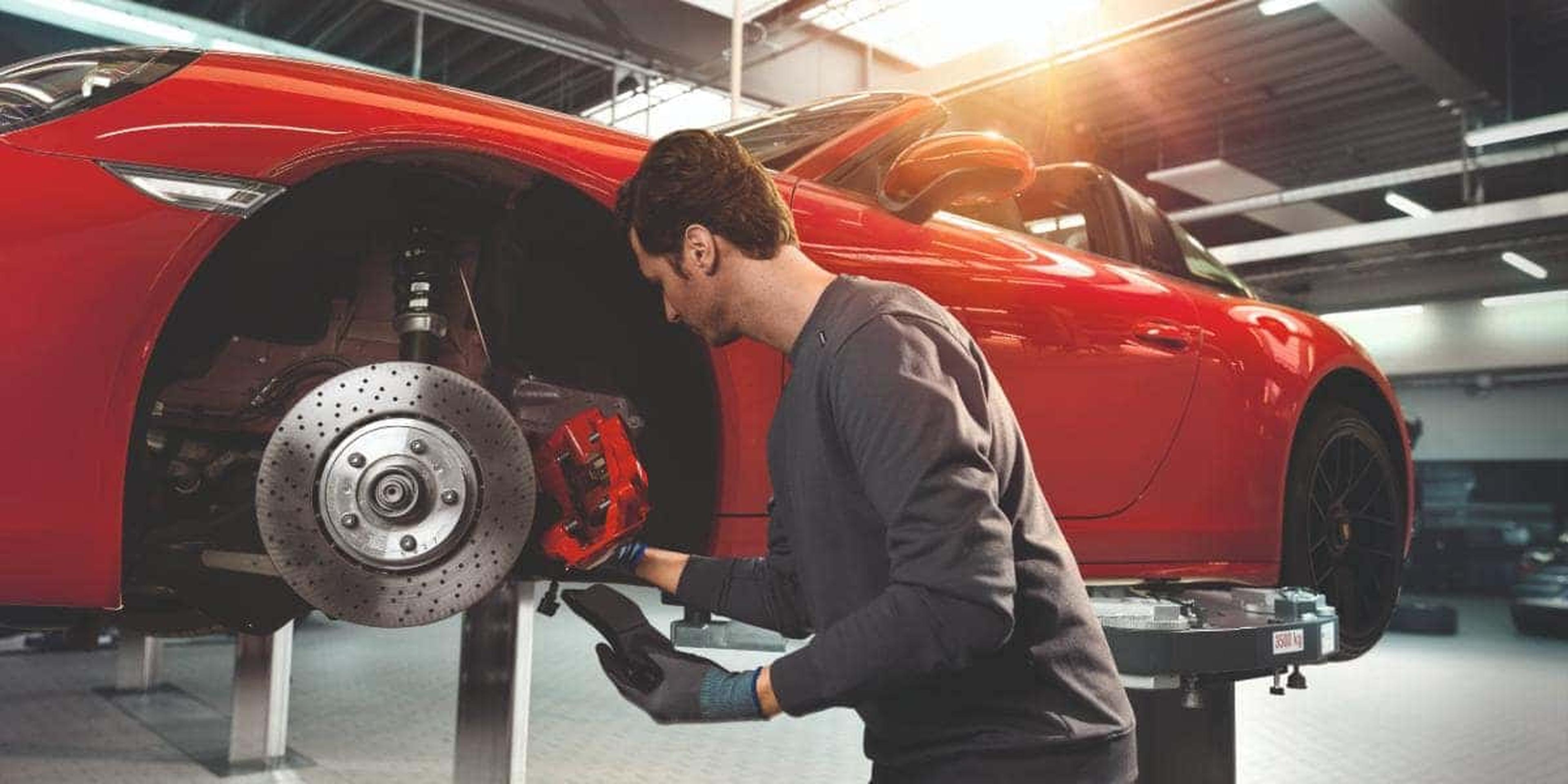 Mechanic working on a red Porsche brake system in a garage.