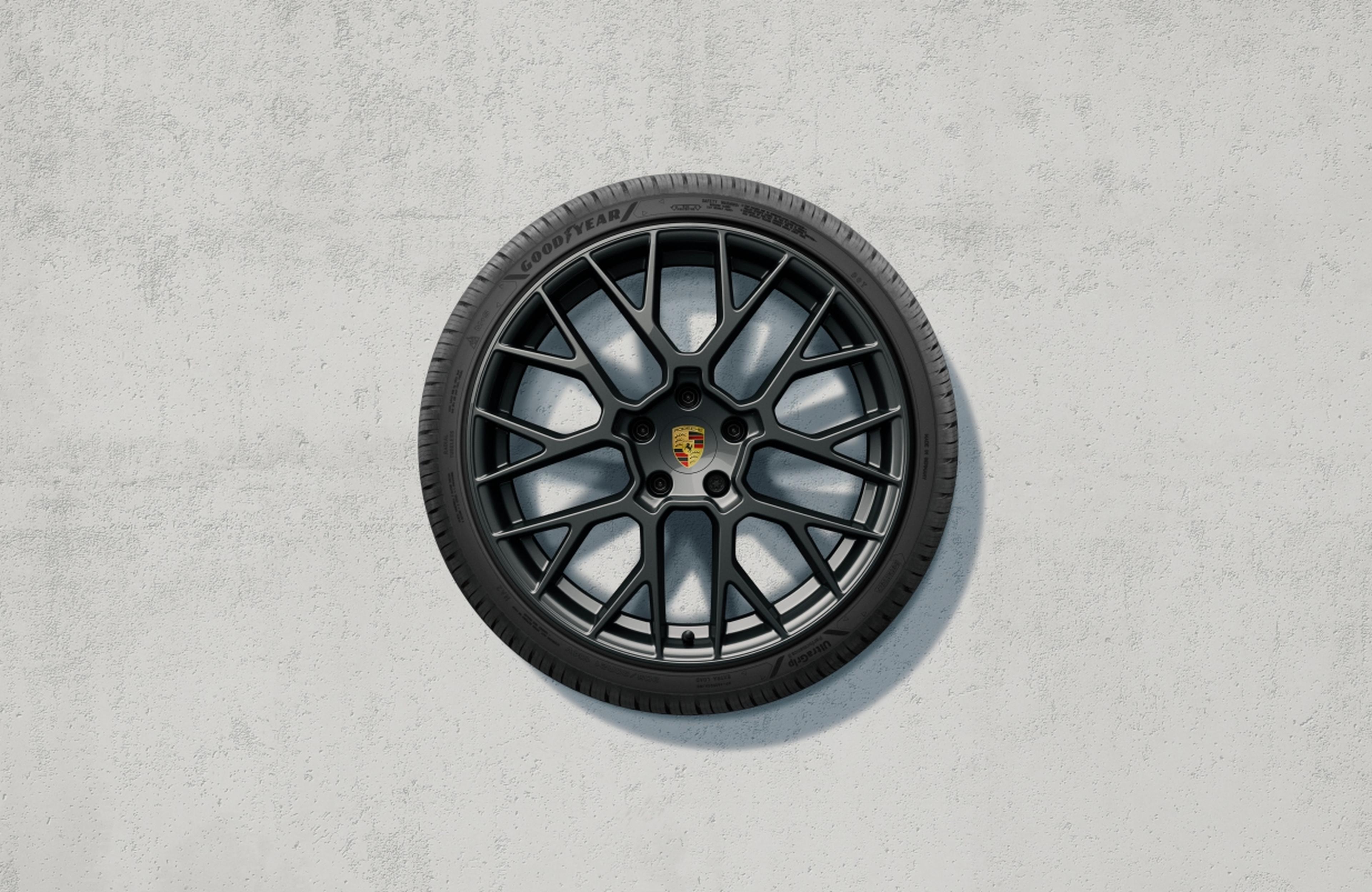 Ein schwarzes Hochleistungs-Leichtmetallrad mit Reifen und zentralem Emblem, montiert an einer strukturierten weißen Wand.