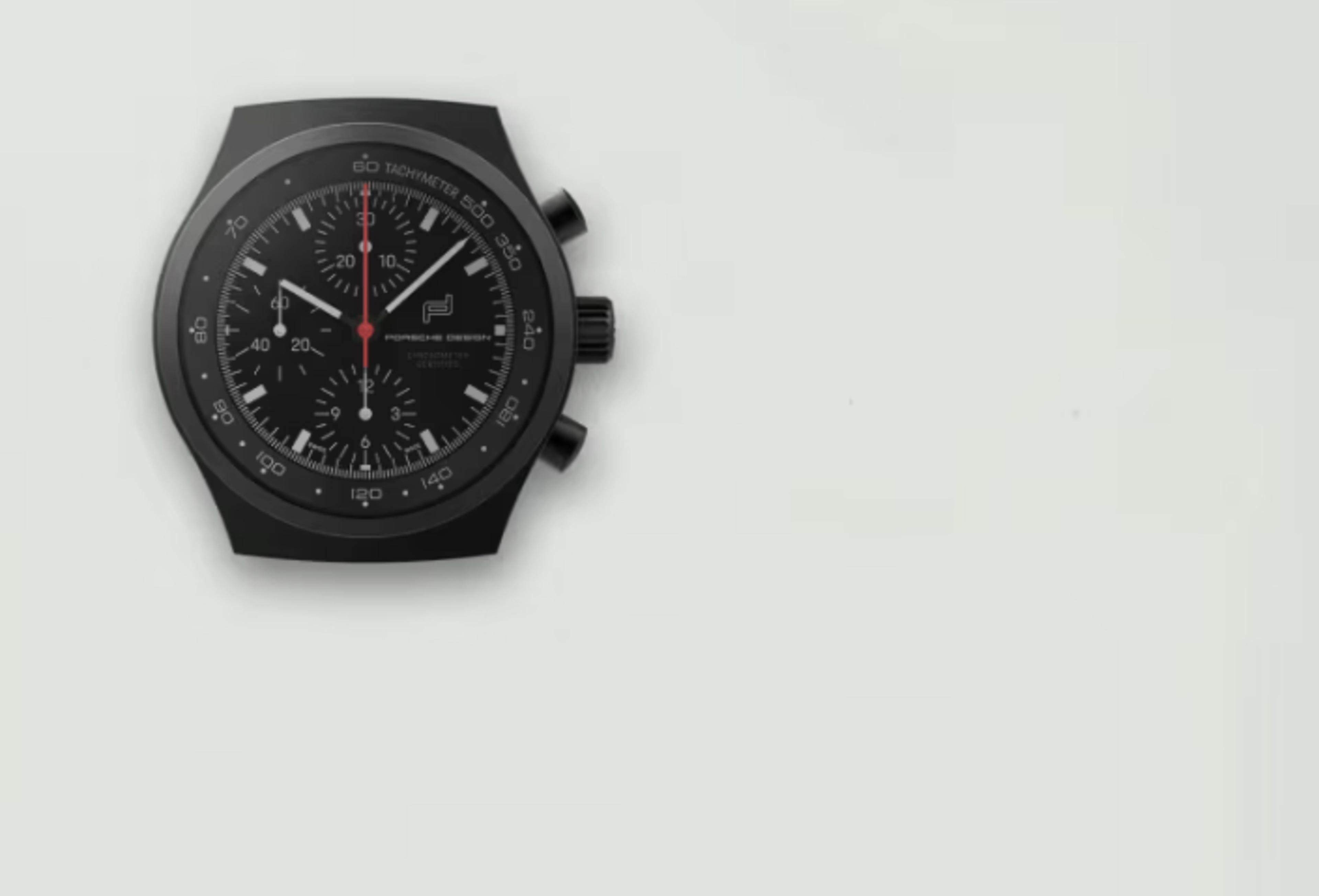 Black chronograph watch with a minimalist design, featuring a dark face, white markers, and red hands, set against a light background.