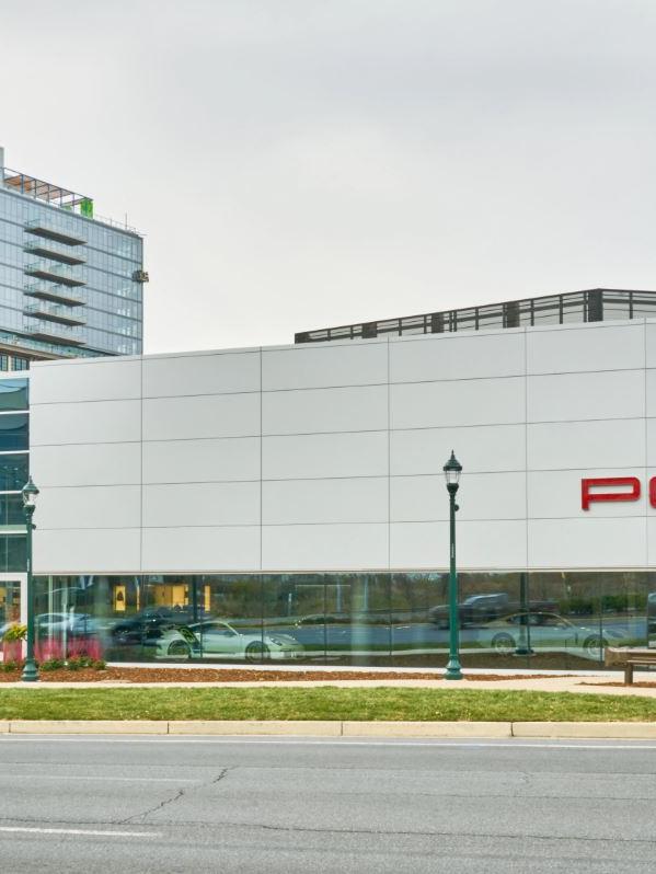 Modern Porsche dealership with a sleek architectural design, situated on a city street with a tall building in the background.