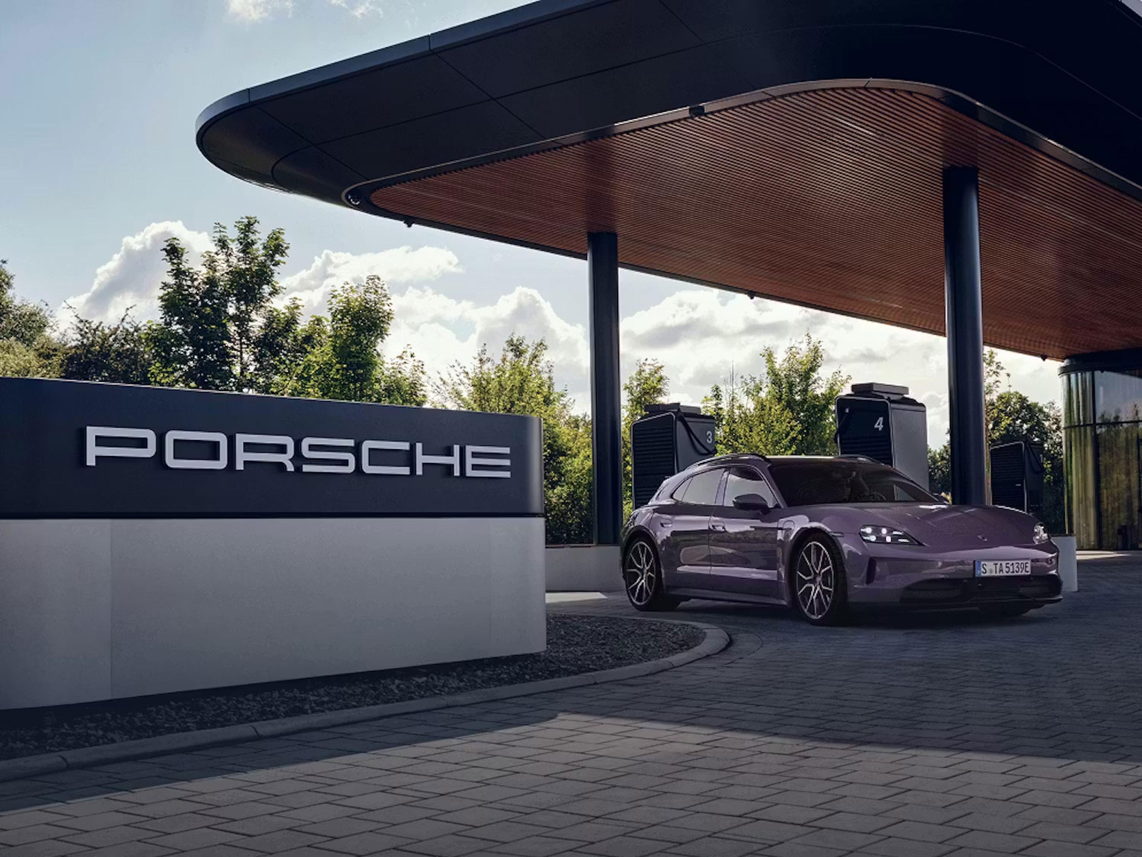 Ein violetter Porsche Taycan lädt an einer eleganten, modernen Ladestation; im Hintergrund sind ein Porsche-Schild und Grünanlagen zu sehen.