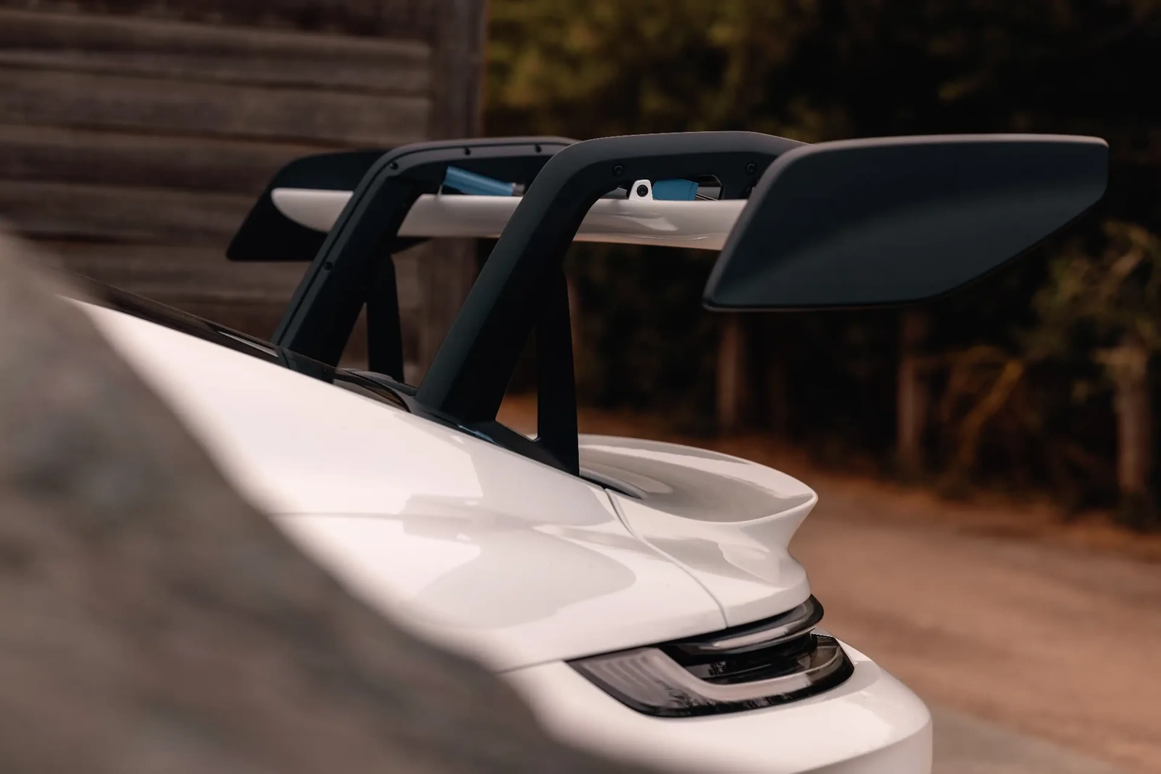 Close-up of a sleek white sports car rear with an aerodynamic black spoiler, set against a blurred natural background.