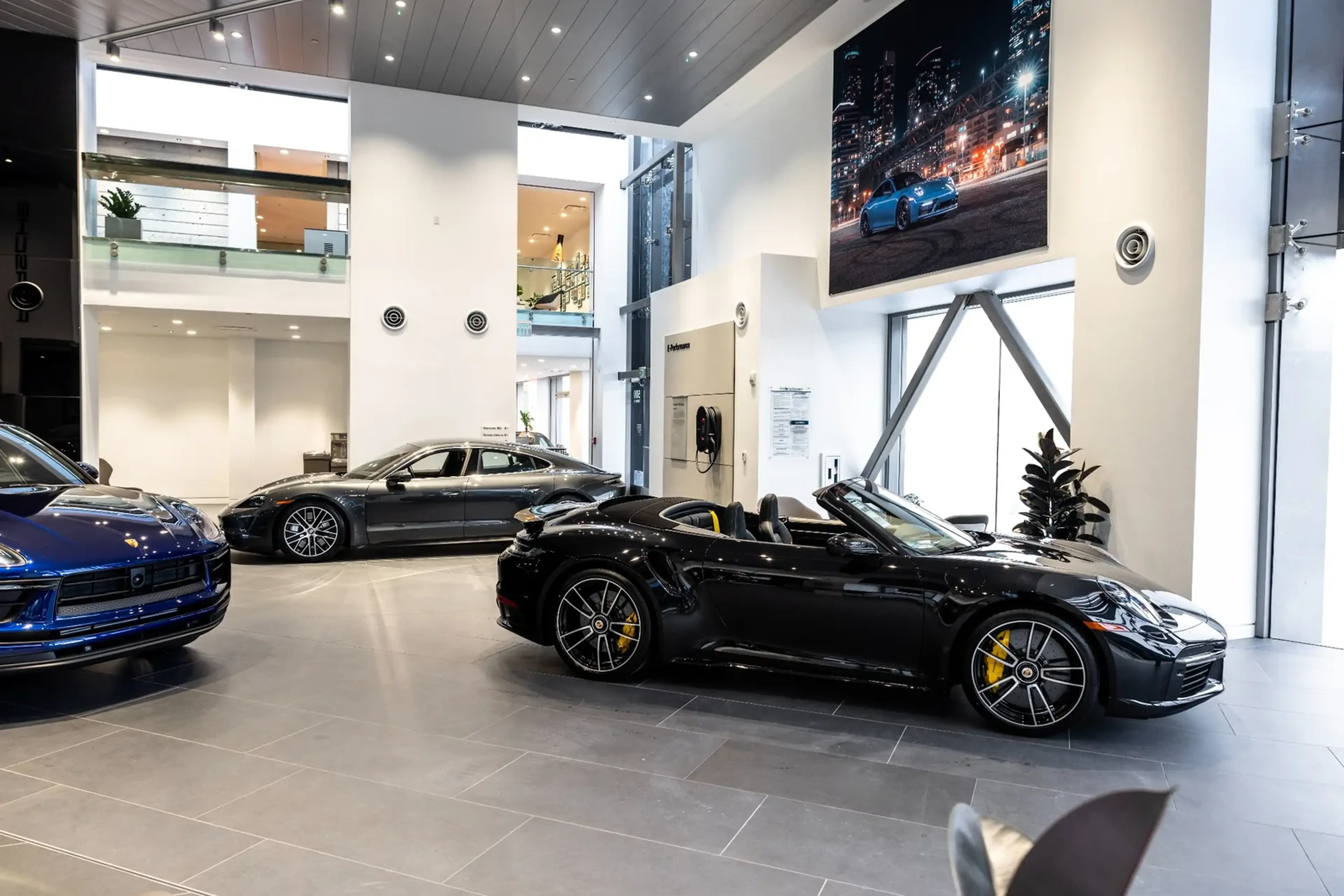 Luxury car showroom featuring three sleek sports cars, including a black convertible in the foreground, with modern decor and bright lighting.