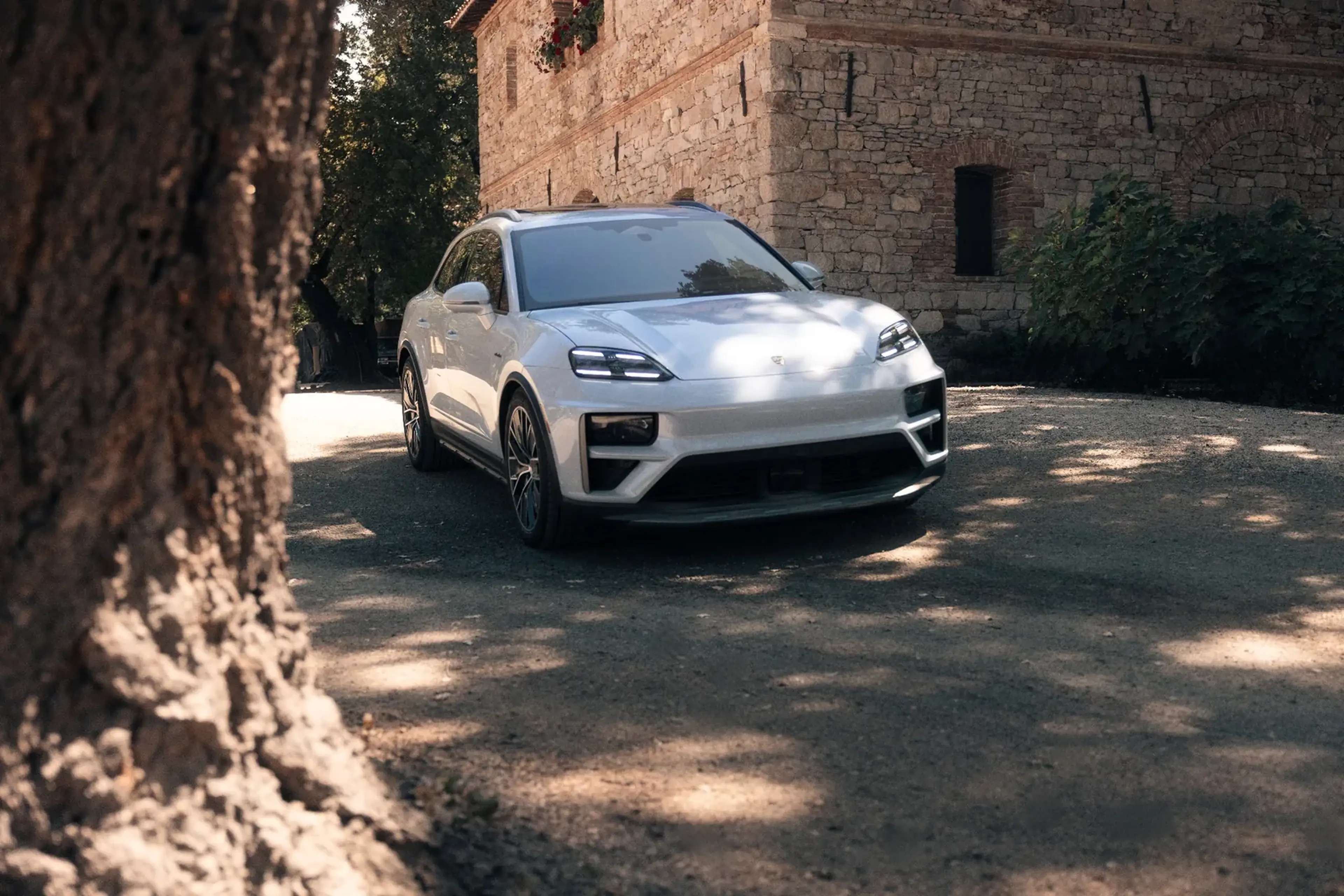 A sleek white SUV parked on a sunlit rustic road, with a stone building and lush greenery in the background.