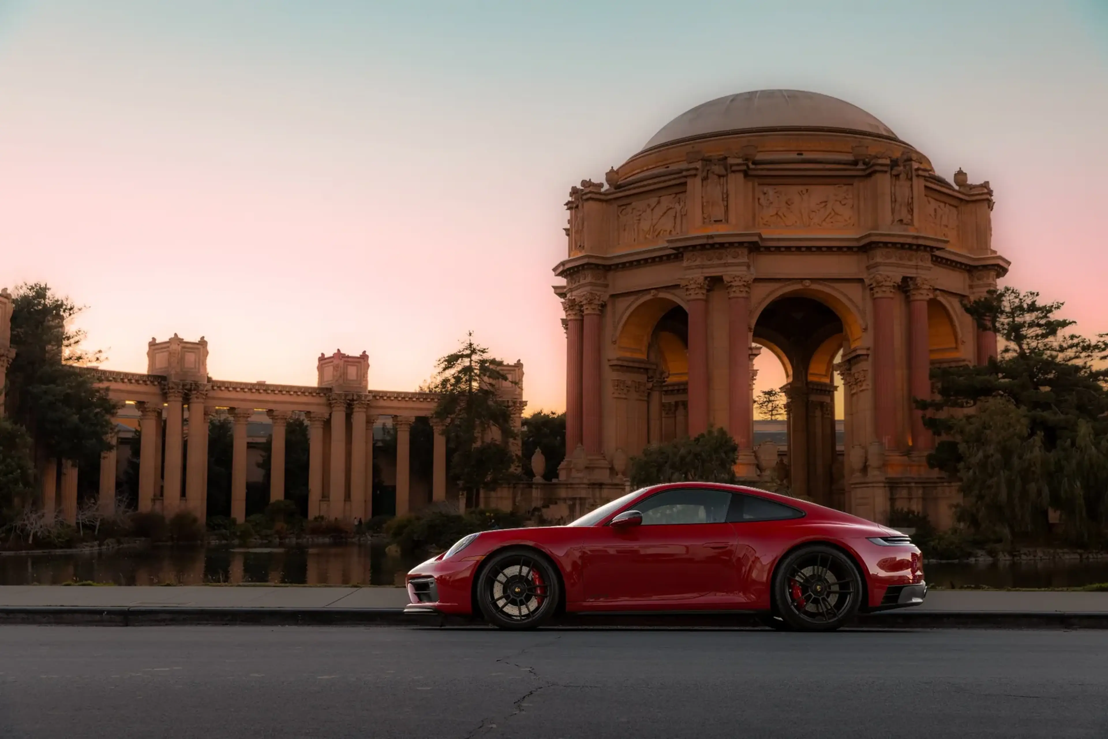 A red sports car parked in front of the Palace of Fine Arts in San Francisco at sunset.