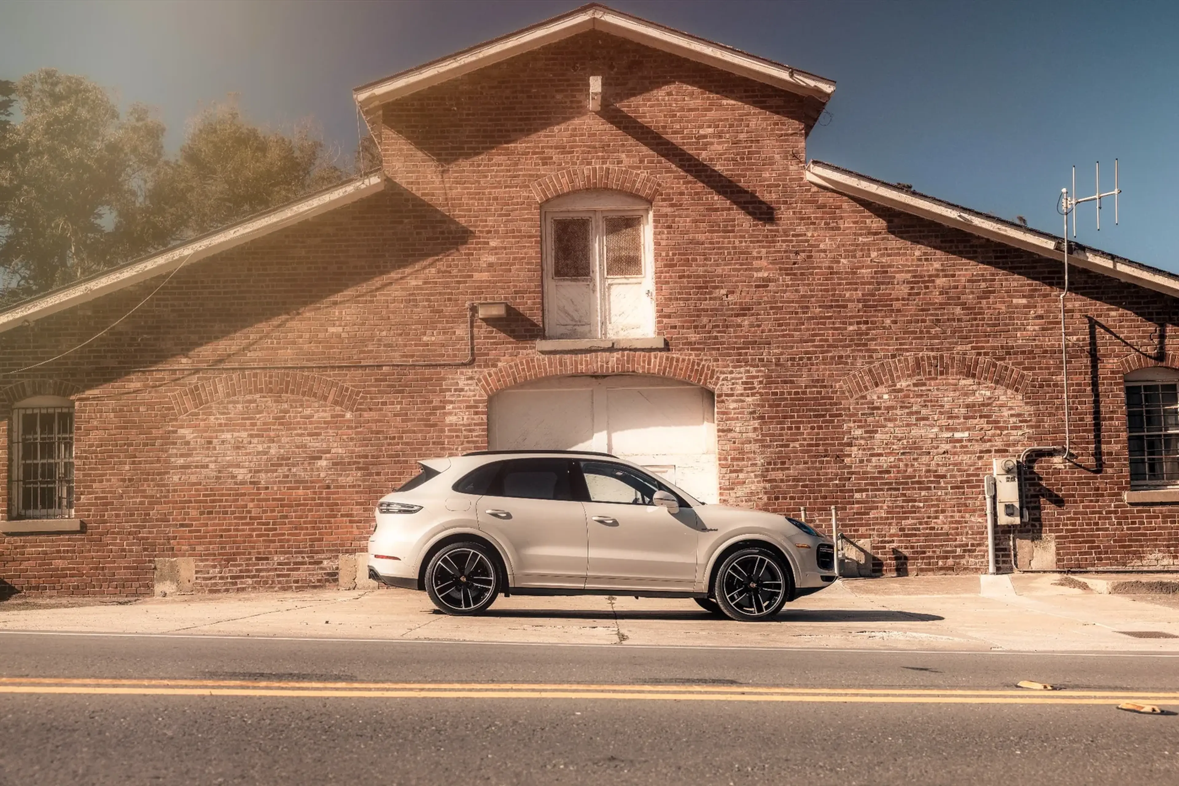 A white SUV parked on a sunny day in front of a brick building with a gabled roof.