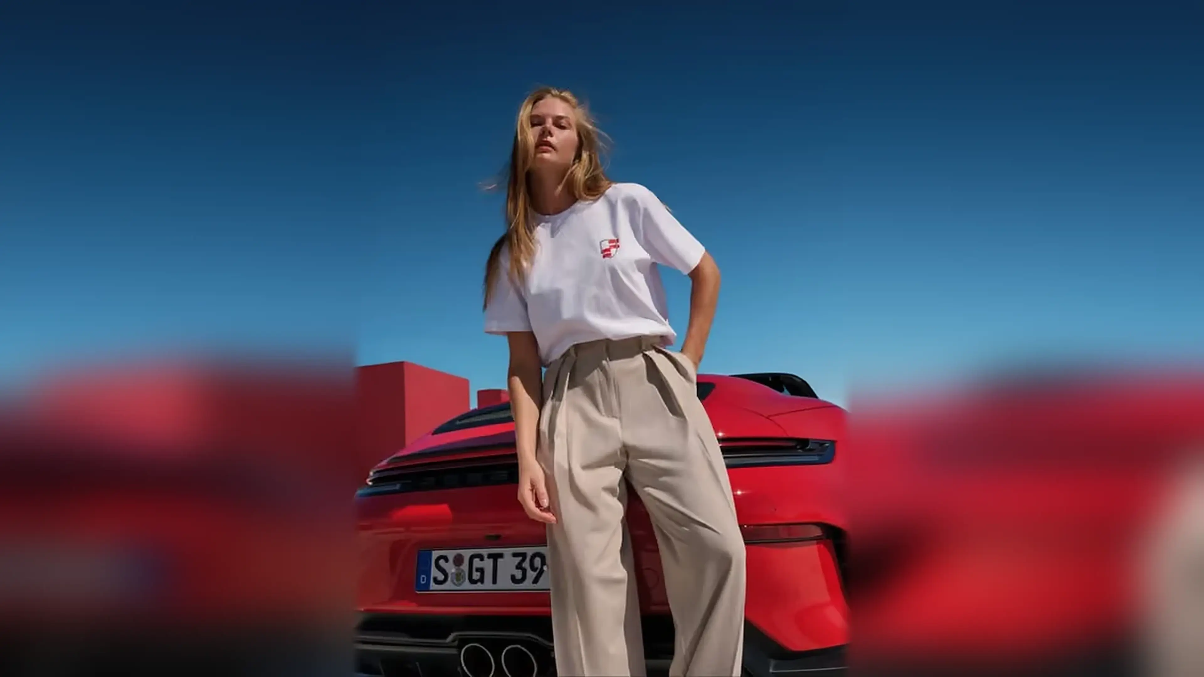 Woman wearing Porsche lifestyle apparel beside a red Porsche.