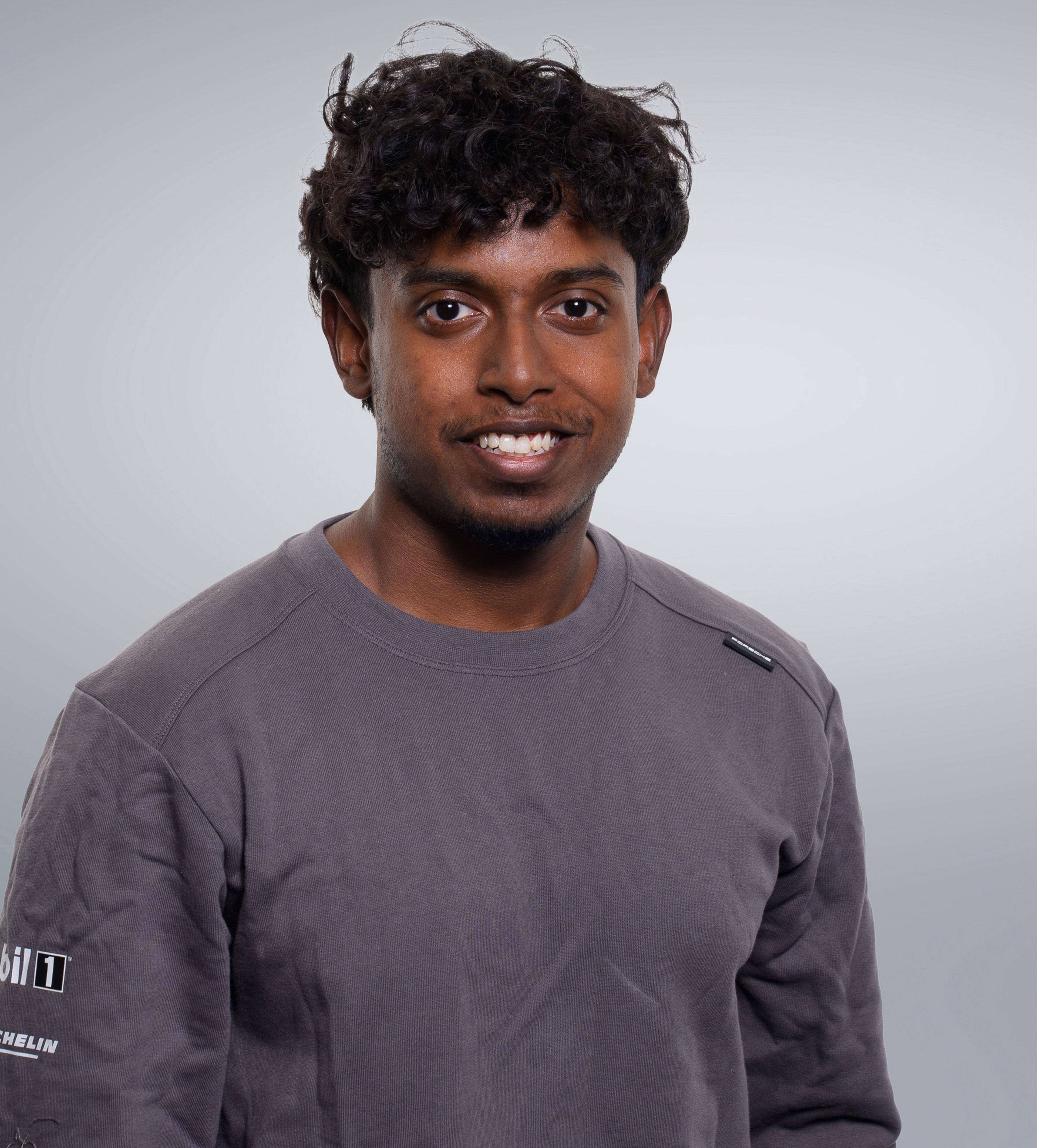 A person with curly hair wearing a gray long-sleeve shirt, smiling at the camera against a plain background.