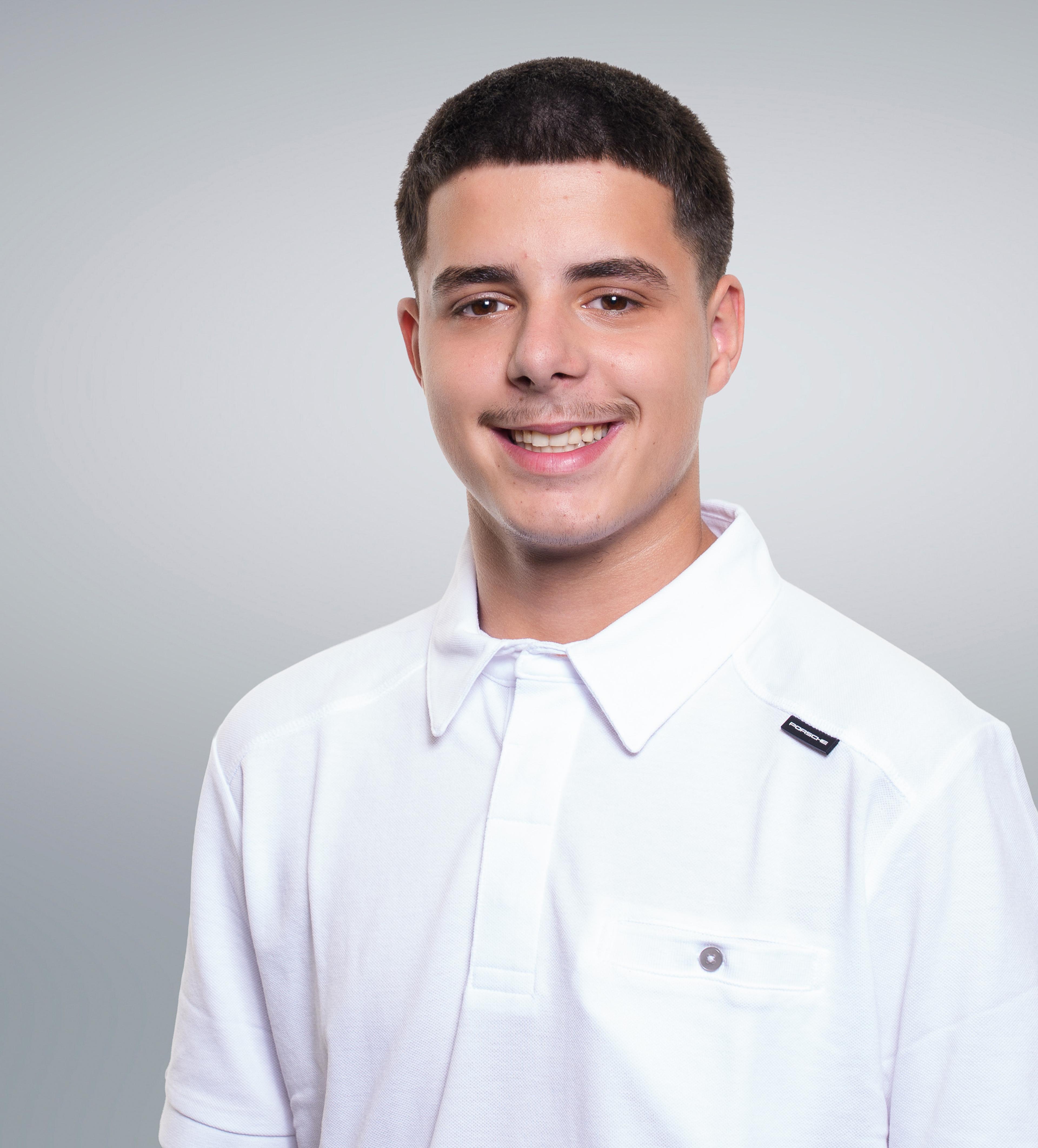 Young man smiling, wearing a white collared shirt, with short dark hair and a light mustache, against a gray background.
