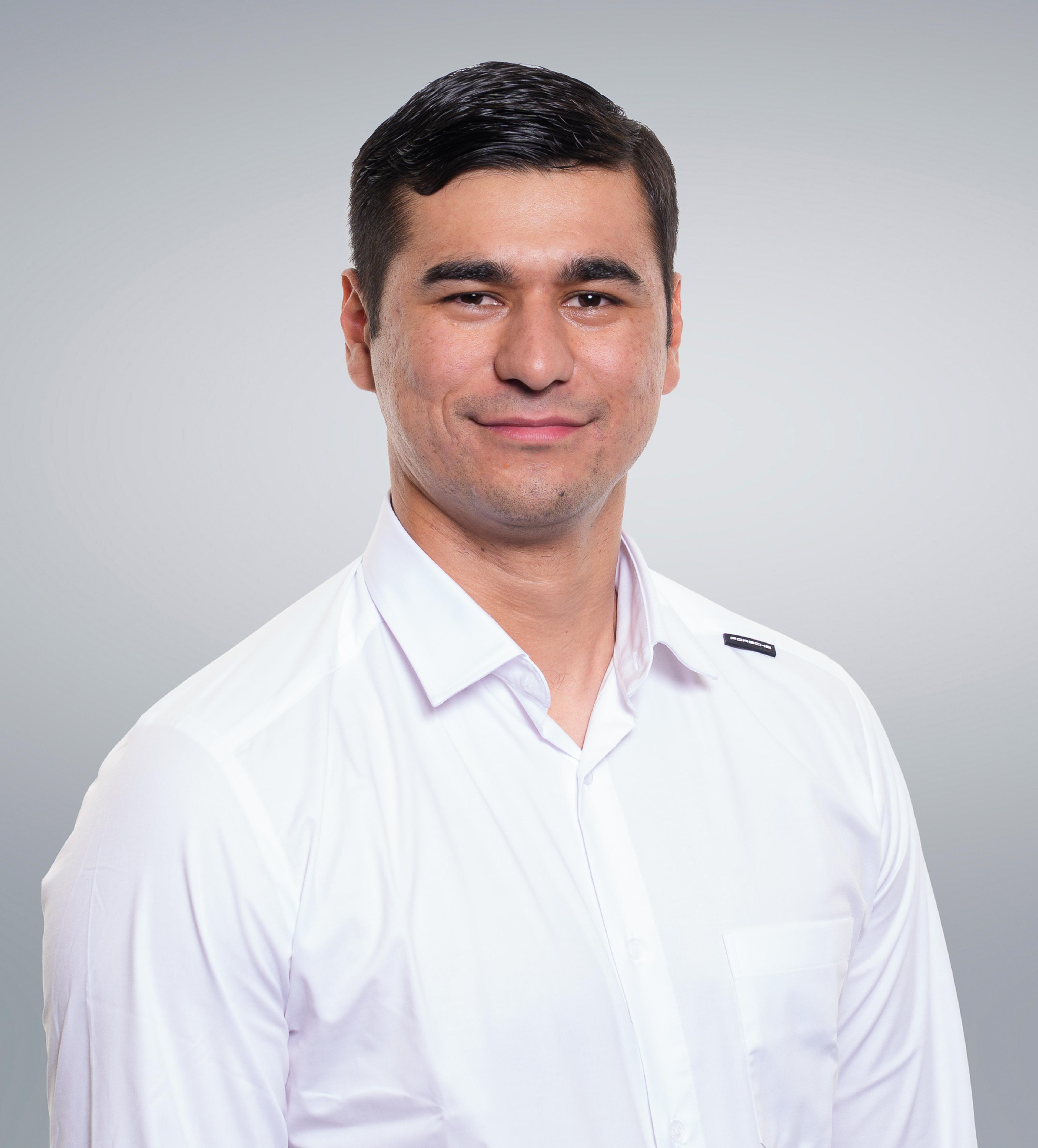 A man in a white button-up shirt smiles at the camera against a plain gray background.