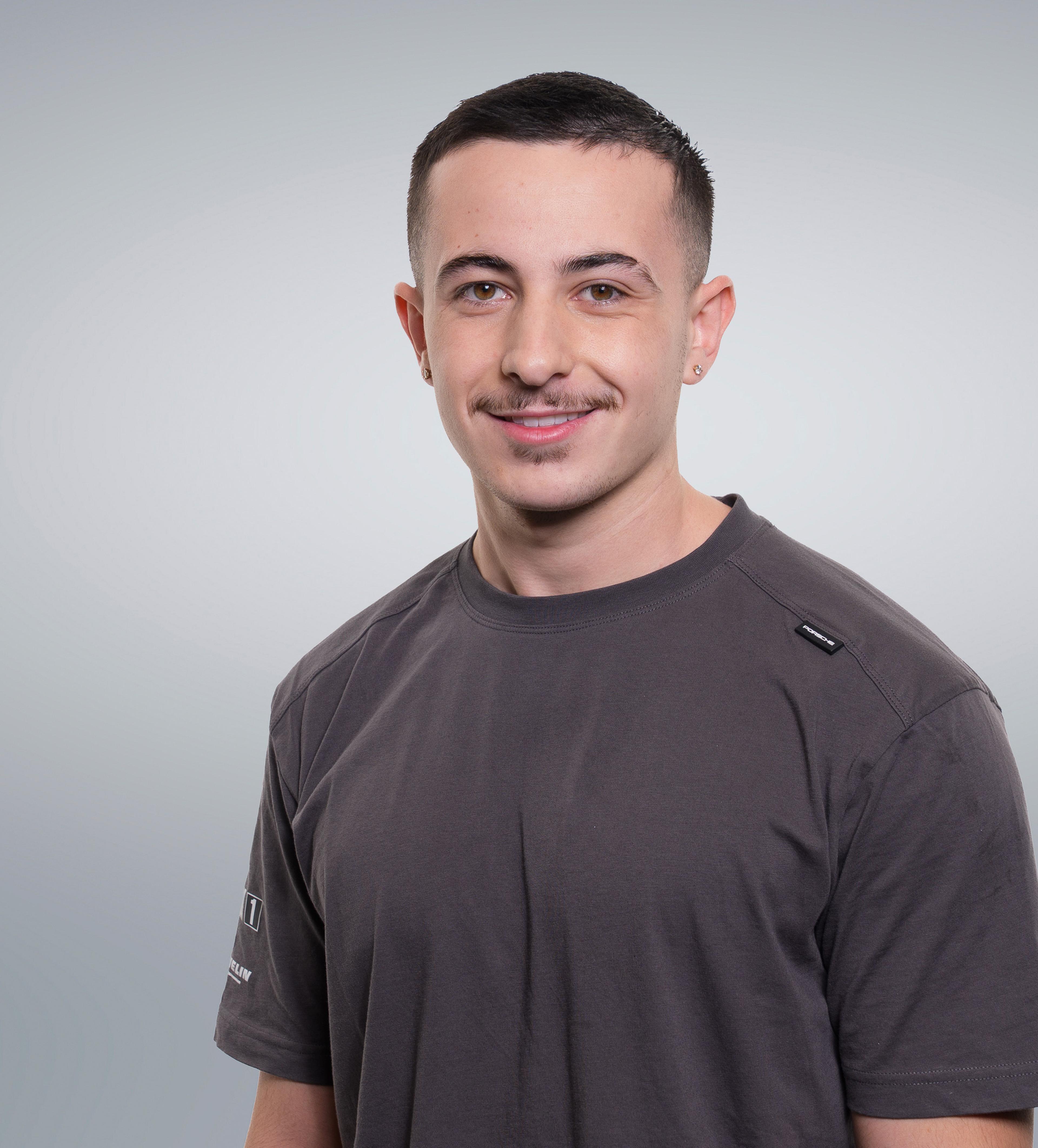 Smiling man with a short haircut and mustache, wearing a grey t-shirt, against a light grey background.