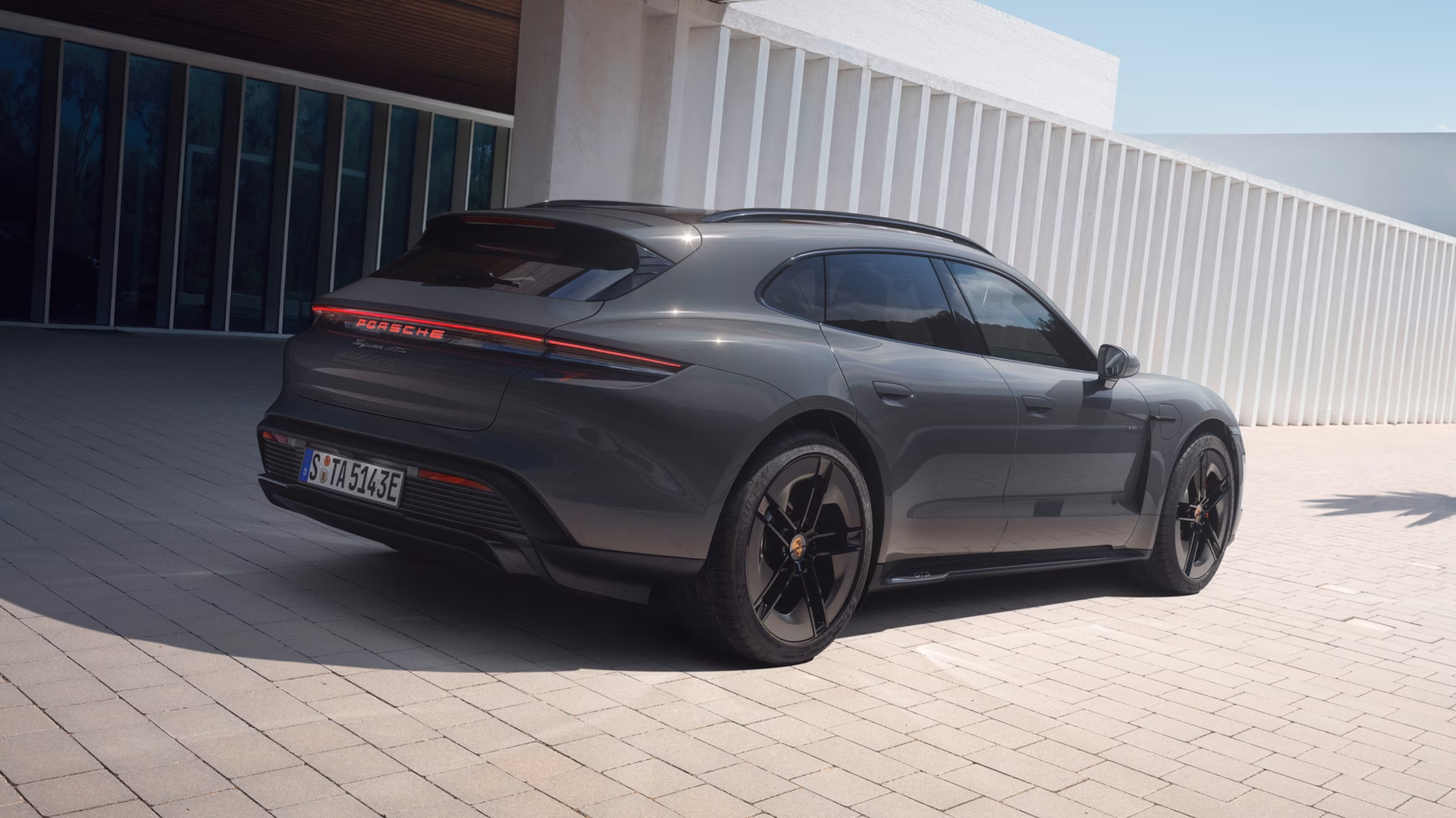 Sleek black sports car parked on a paved surface outside a modern white building with large windows and vertical slats.