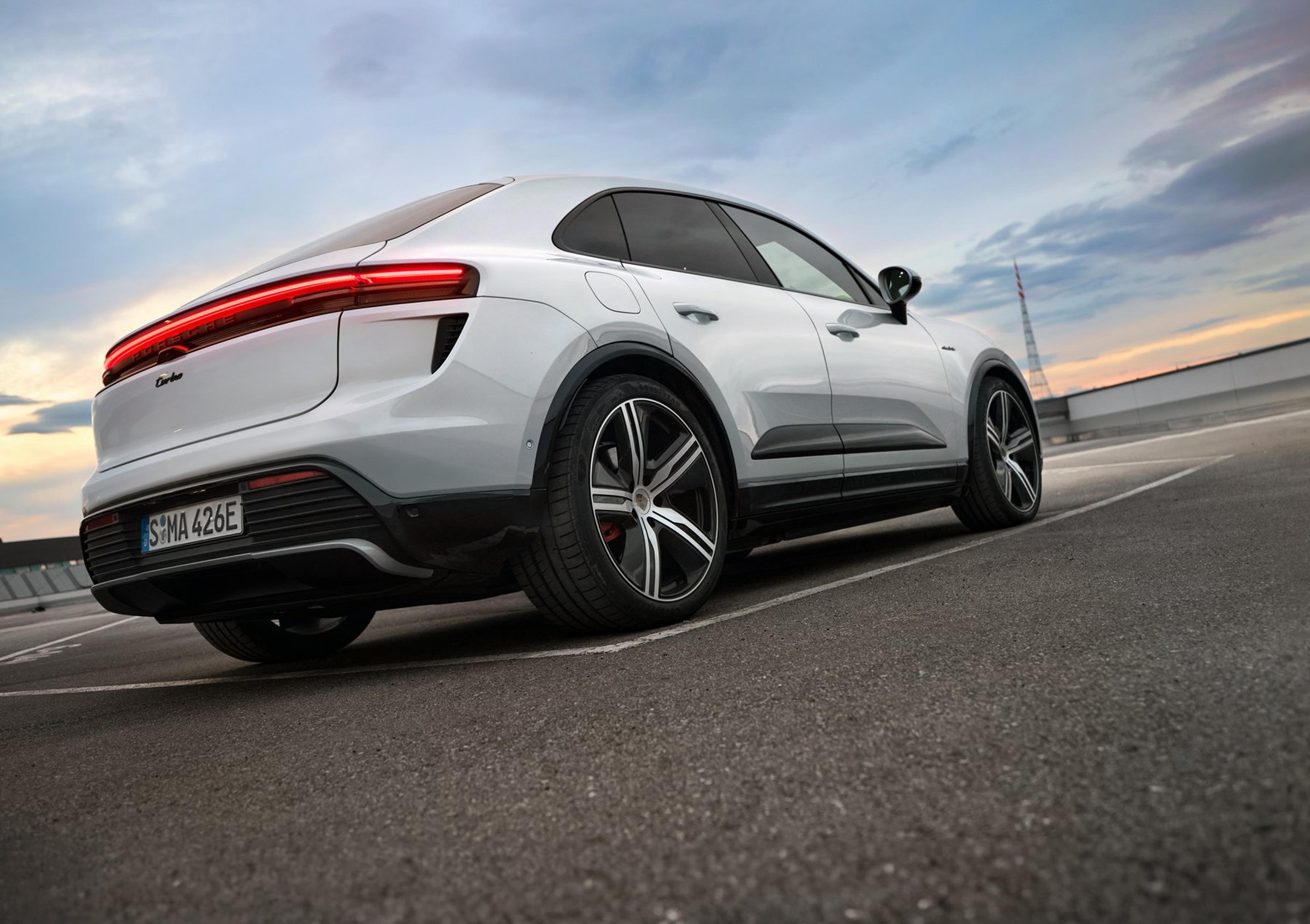 Rear three-quarter view of a white 2026 Porsche Macan Turbo Electric with full-width light bar at sunset