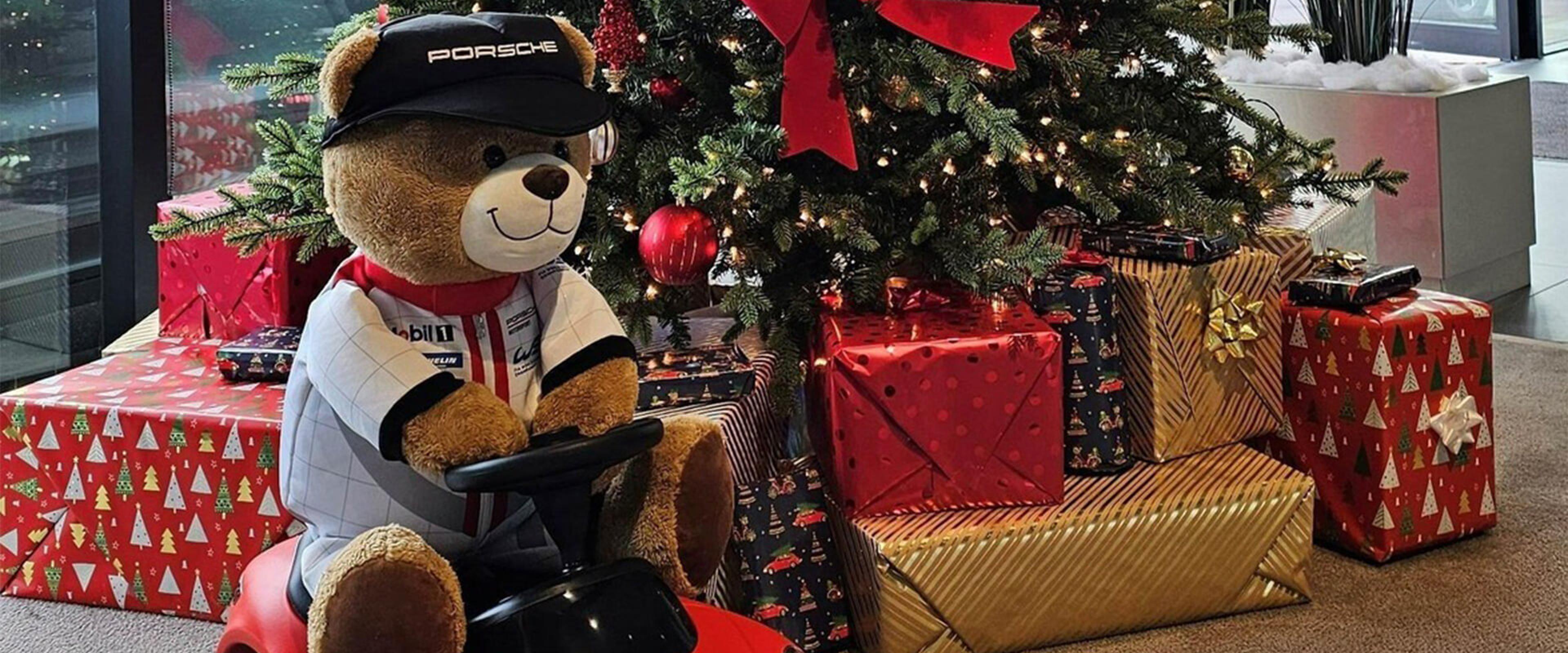 Teddy bear wearing Porsche hat with presents under a tree