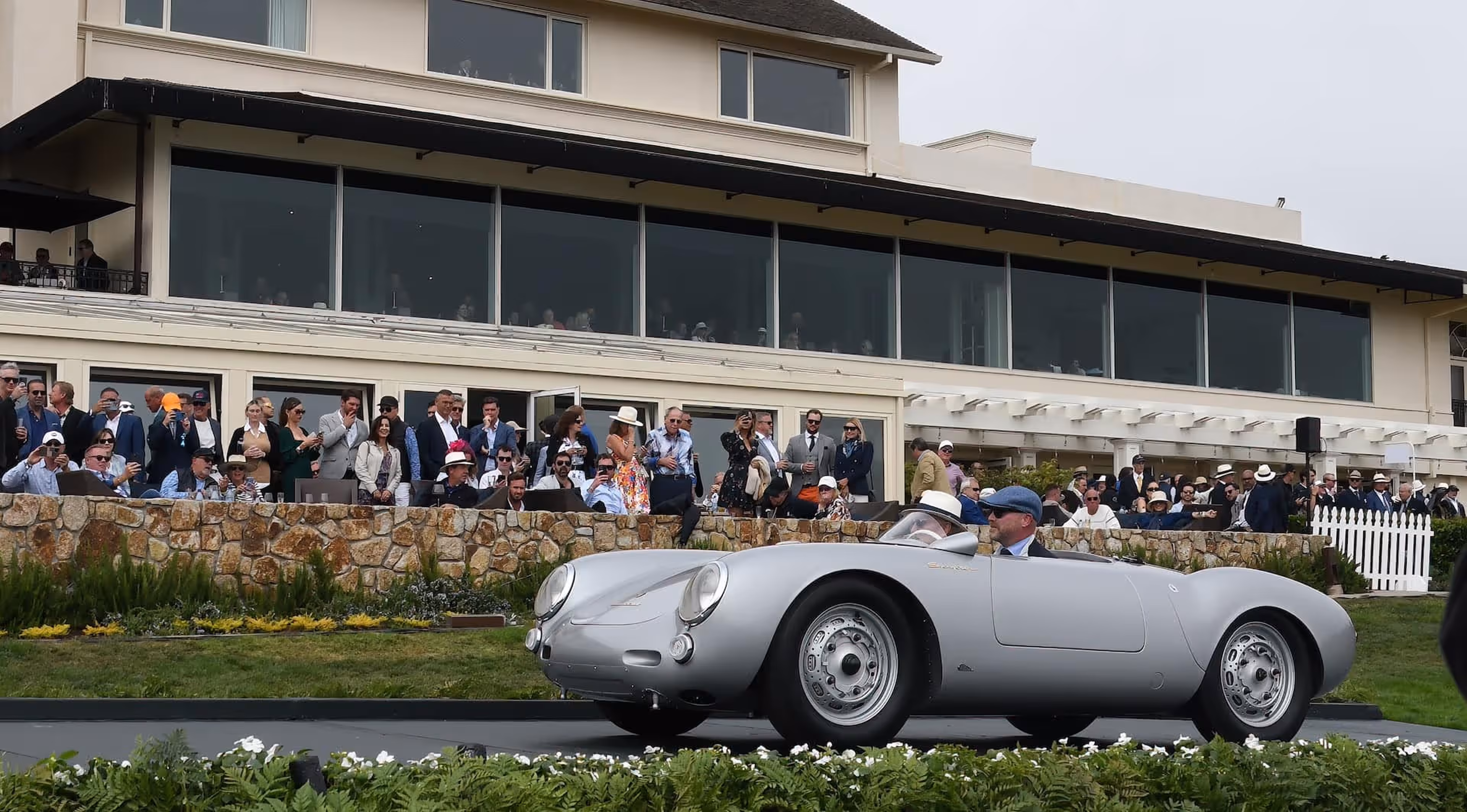 Porsche oldtimer in grey driving past a crowd.