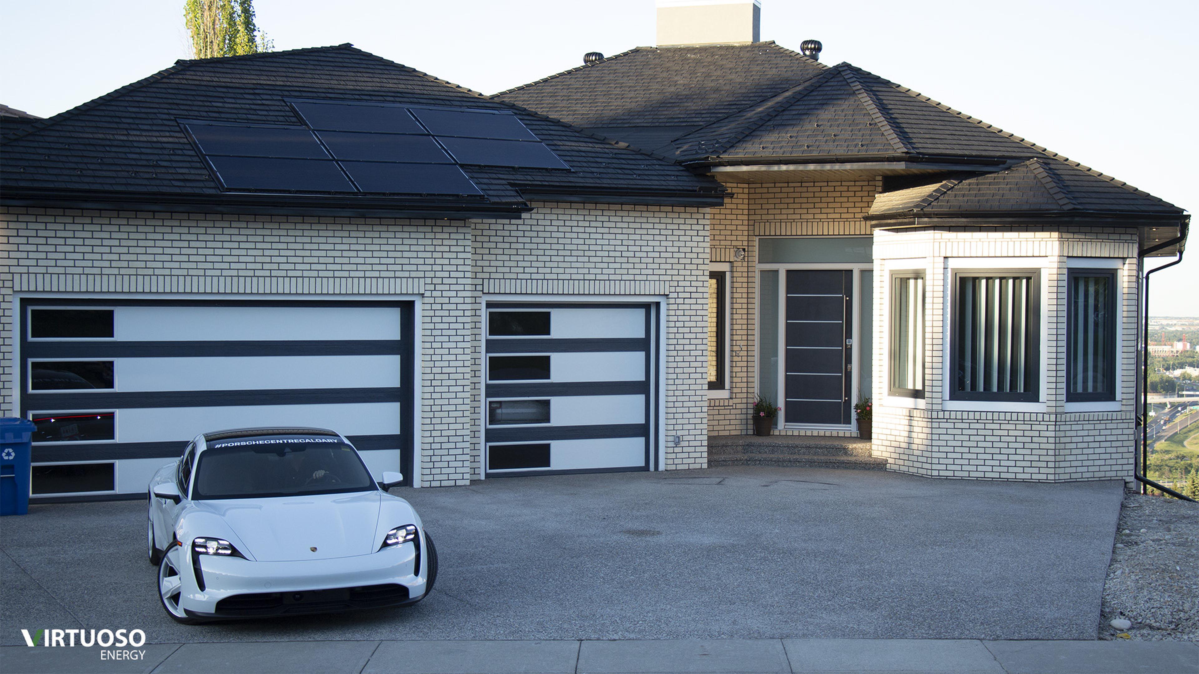 A modern house with solar panels on the roof and a Taycan parked in the driveway. The garage doors feature horizontal windows.