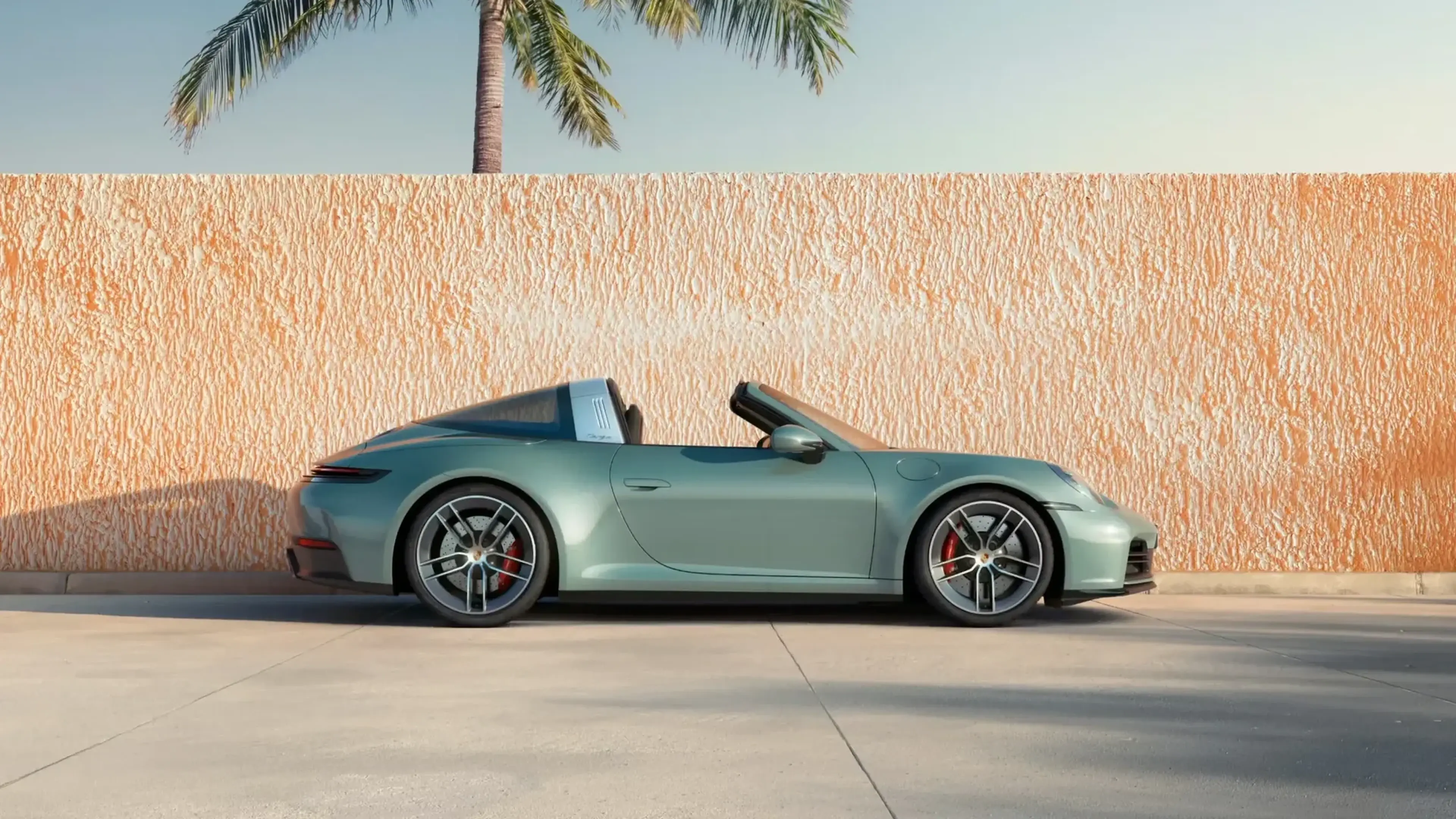 Side view of a Porsche 911 Targa with the roof open, parked in front of a textured wall.