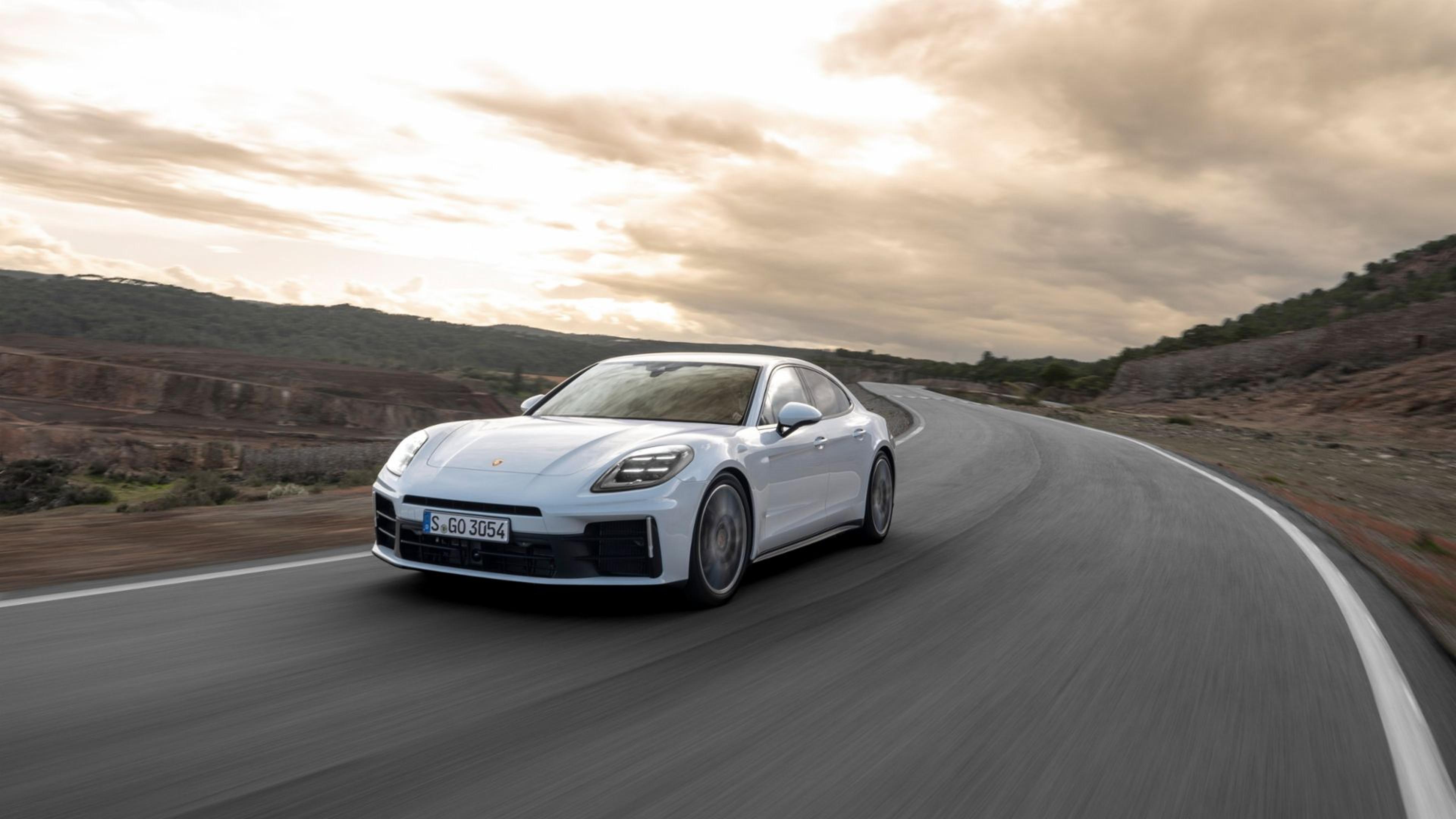 Porsche Panamera 4 driving on a winding road with a scenic, hilly landscape and cloudy sky in the background.