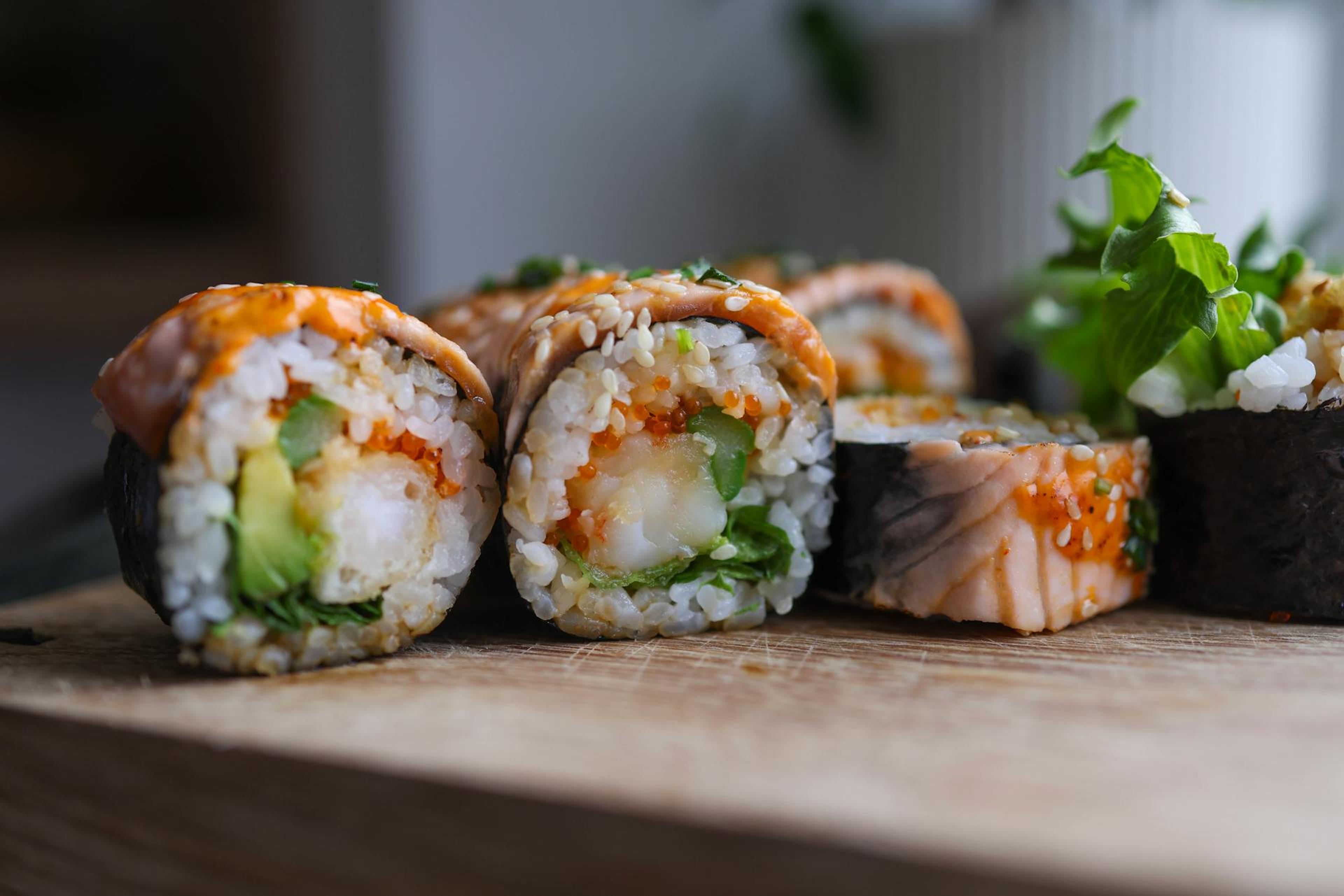 Close-up of sushi rolls on a wooden board, filled with shrimp, avocado, and cucumber