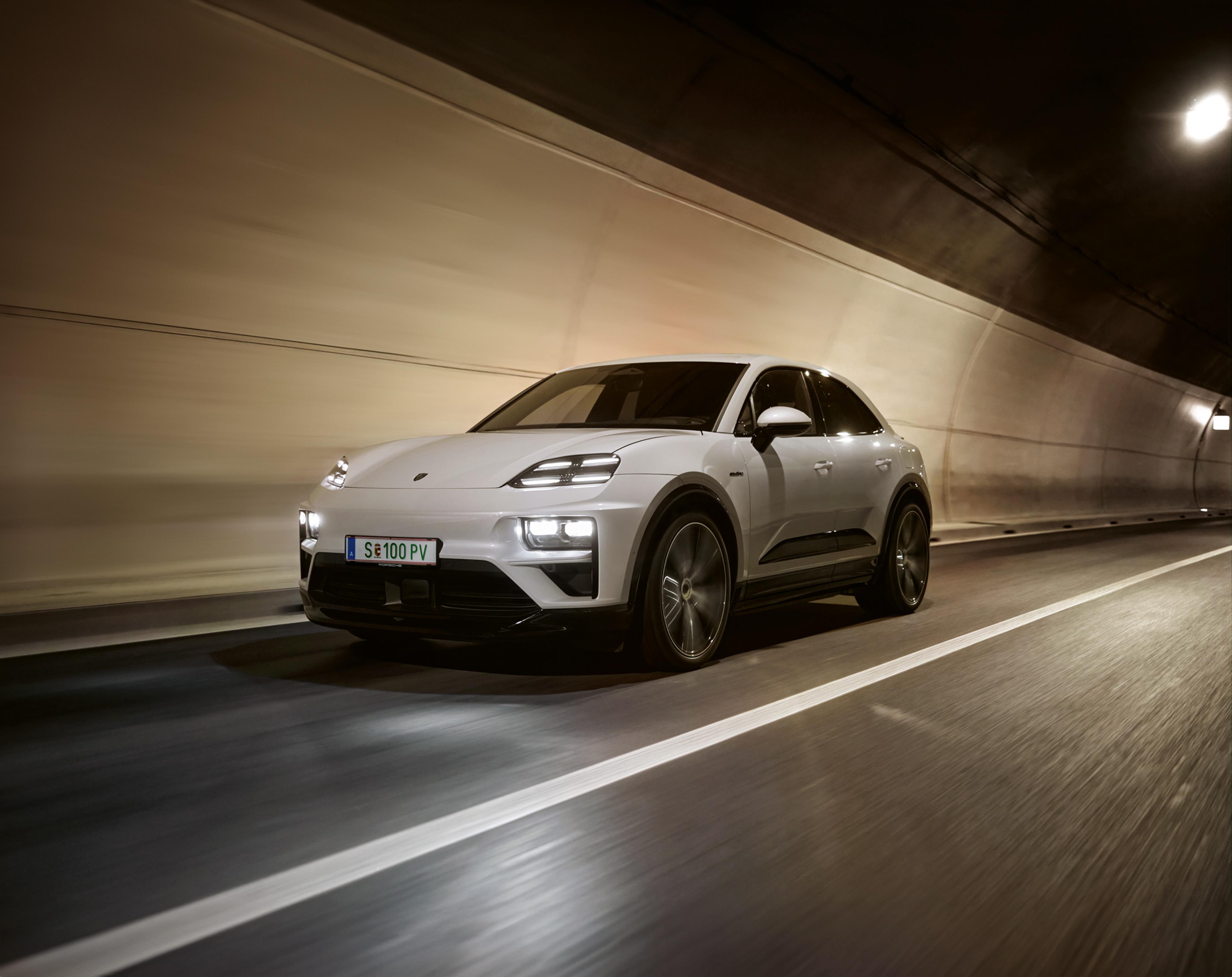 Ein eleganter, weißer Porsche Macan fährt mit eingeschalteten Scheinwerfern durch einen schwach beleuchteten Tunnel, die Bewegungsunschärfe vermittelt den Eindruck von Geschwindigkeit.