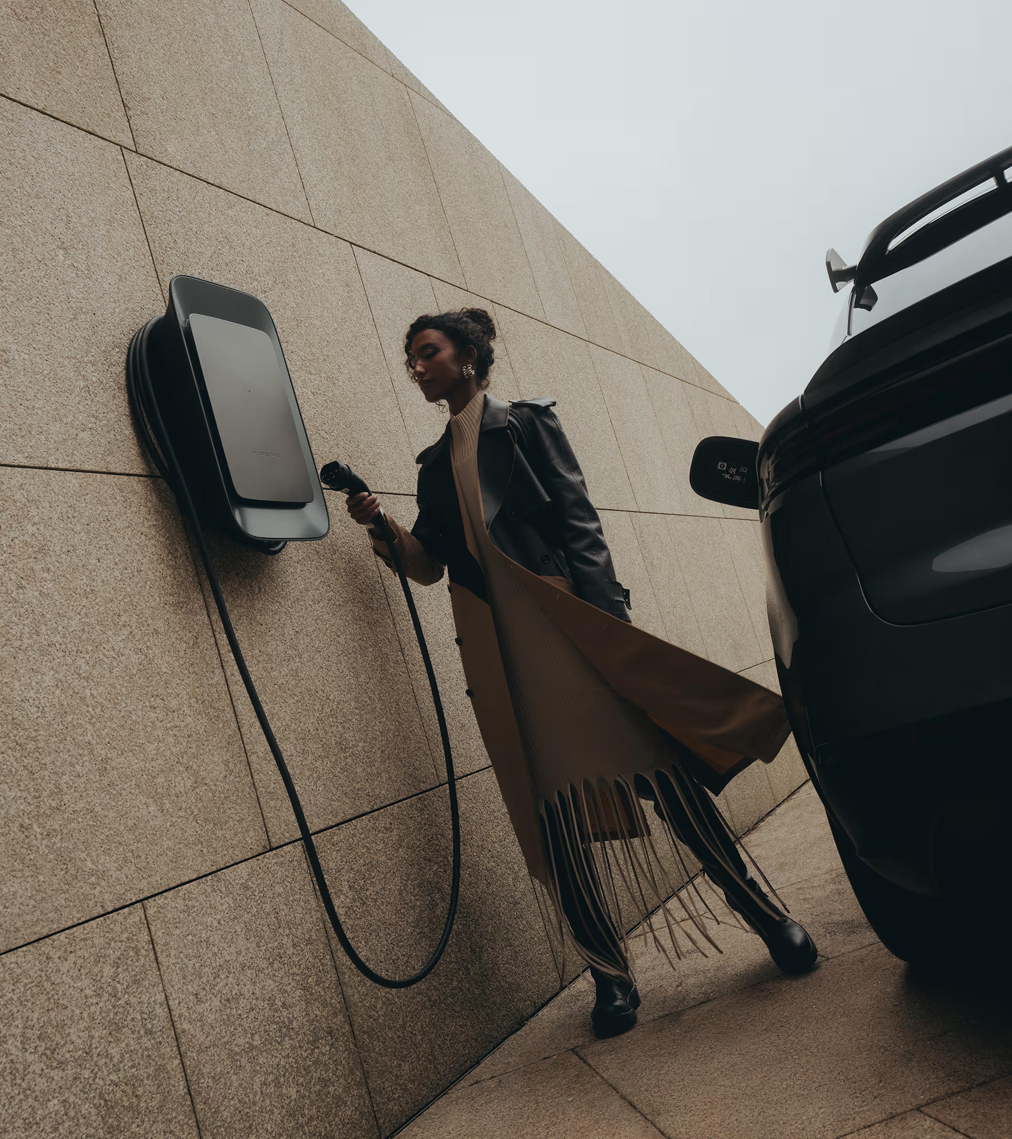 Frau steht neben einem Porsche Fahrzeug und bedient eine graue Wallbox.