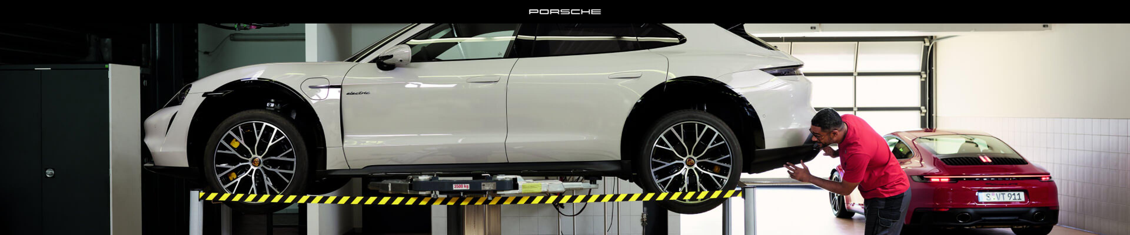 Side view of a Porsche Taycan Cross Turismo in White with a mechanic examining the rear bumper.