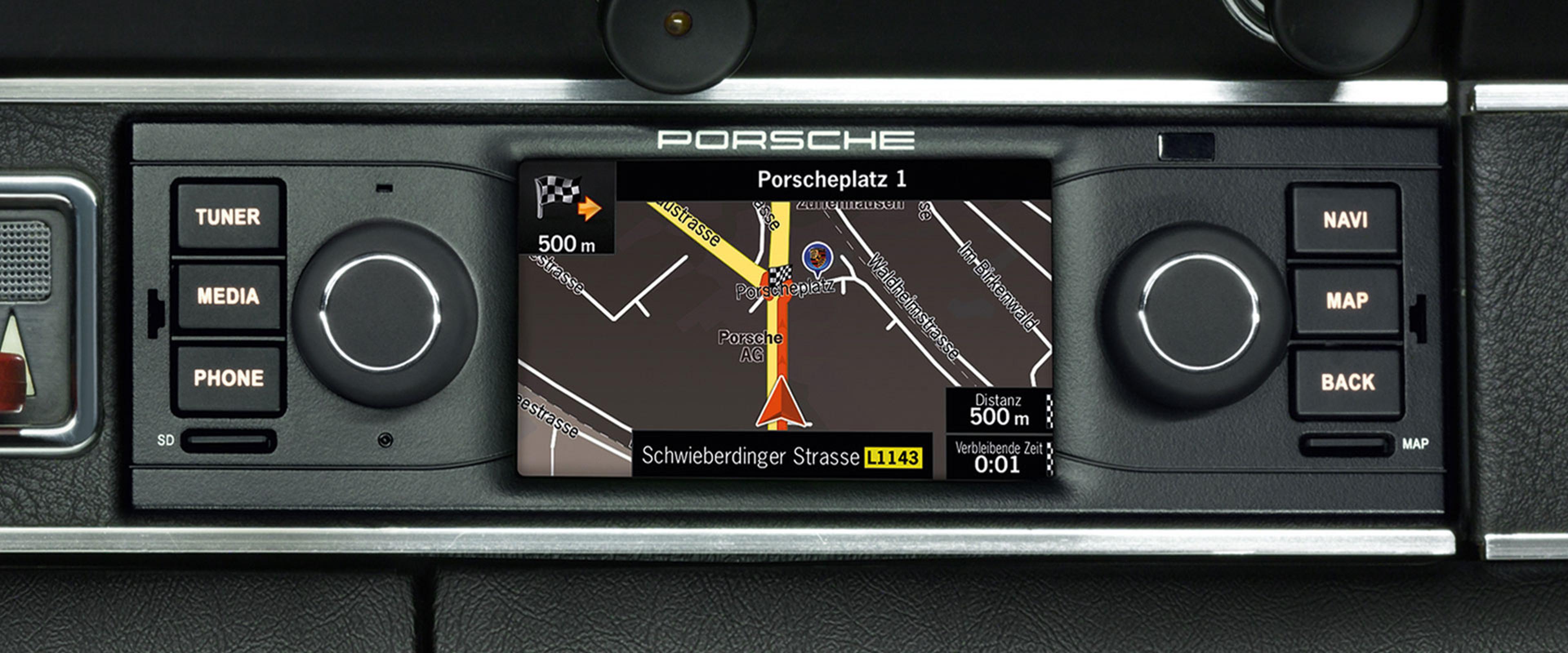 Car GPS navigation display showing a route to Porscheplatz 1, with street names and directional controls on the device.